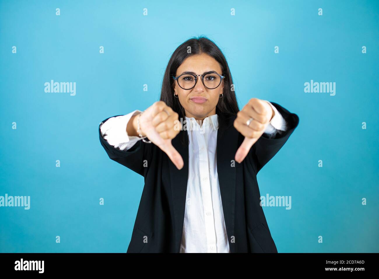 Junge schöne Geschäftsfrau über isolierten blauen Hintergrund mit wütenden Gesicht, negative Zeichen zeigt Abneigung mit Daumen nach unten Stockfoto