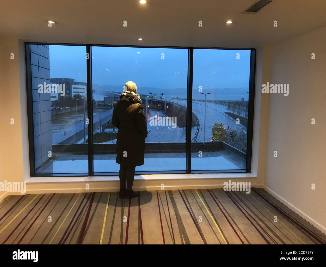 Frau steht an einem regnerischen Tag in Dundee vor einem großen Fenster Stockfoto
