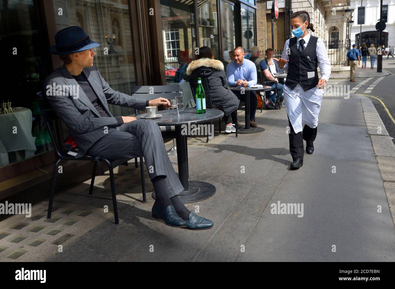 London, England, Großbritannien. Mann sitzt vor einem Café - Kellnerin trägt eine Gesichtsmaske, während der COVID Pandemie, August 2020 Stockfoto