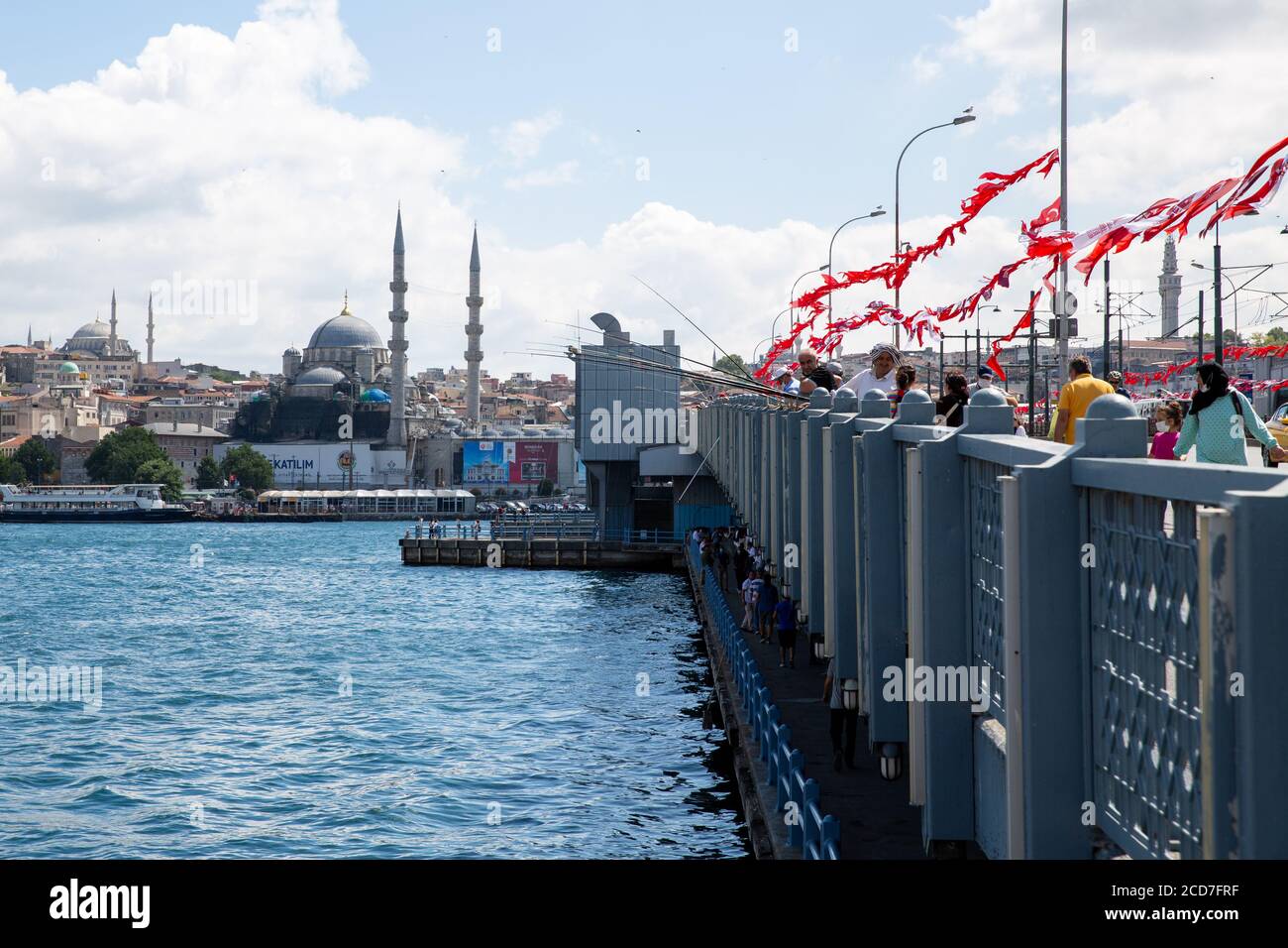 ISTANBUL / TÜRKEI - 07.17.2020: Menschen fischen auf der Golden Horn (Halic) Brücke, der Yeni Moschee und dem Beyazit Turm im Hintergrund, Eminonu. Stockfoto