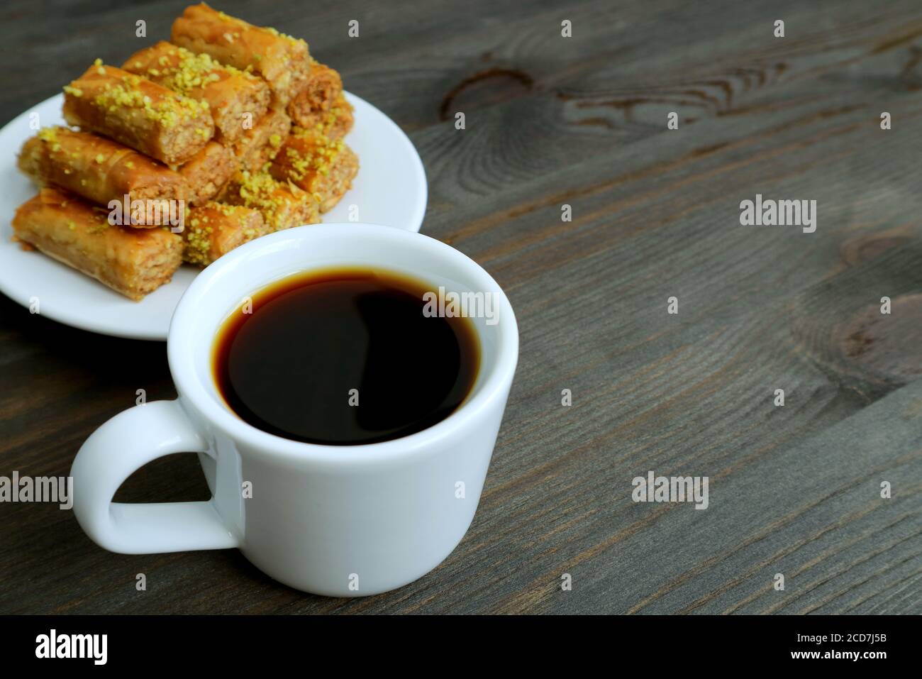 Tasse türkischer Kaffee auf Holztisch mit verschwommener Pistazie Nüsse Baklava Gebäck im Hintergrund Stockfoto