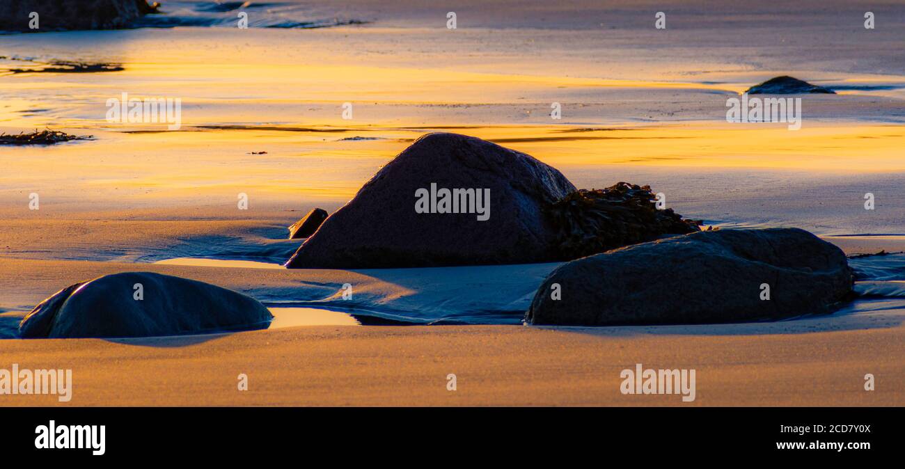 Orangefarbener Sonnenuntergang am Sandstrand mit hinterleuchteten Felsen Stockfoto