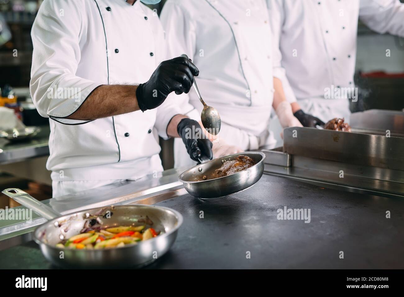Köche in Schutzmasken und Handschuhen bereiten Essen in der Küche eines Restaurants oder Hotels zu. Stockfoto