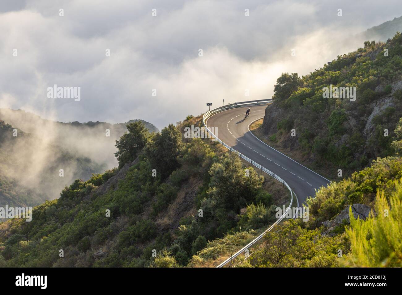 Straße verschlungen Bergstraße mit einem Radfahrer in der Ferne zwischen den Wolken, Sant Pere de Rodes, Costa Brava, Girona, Katalonien, Spanien Stockfoto