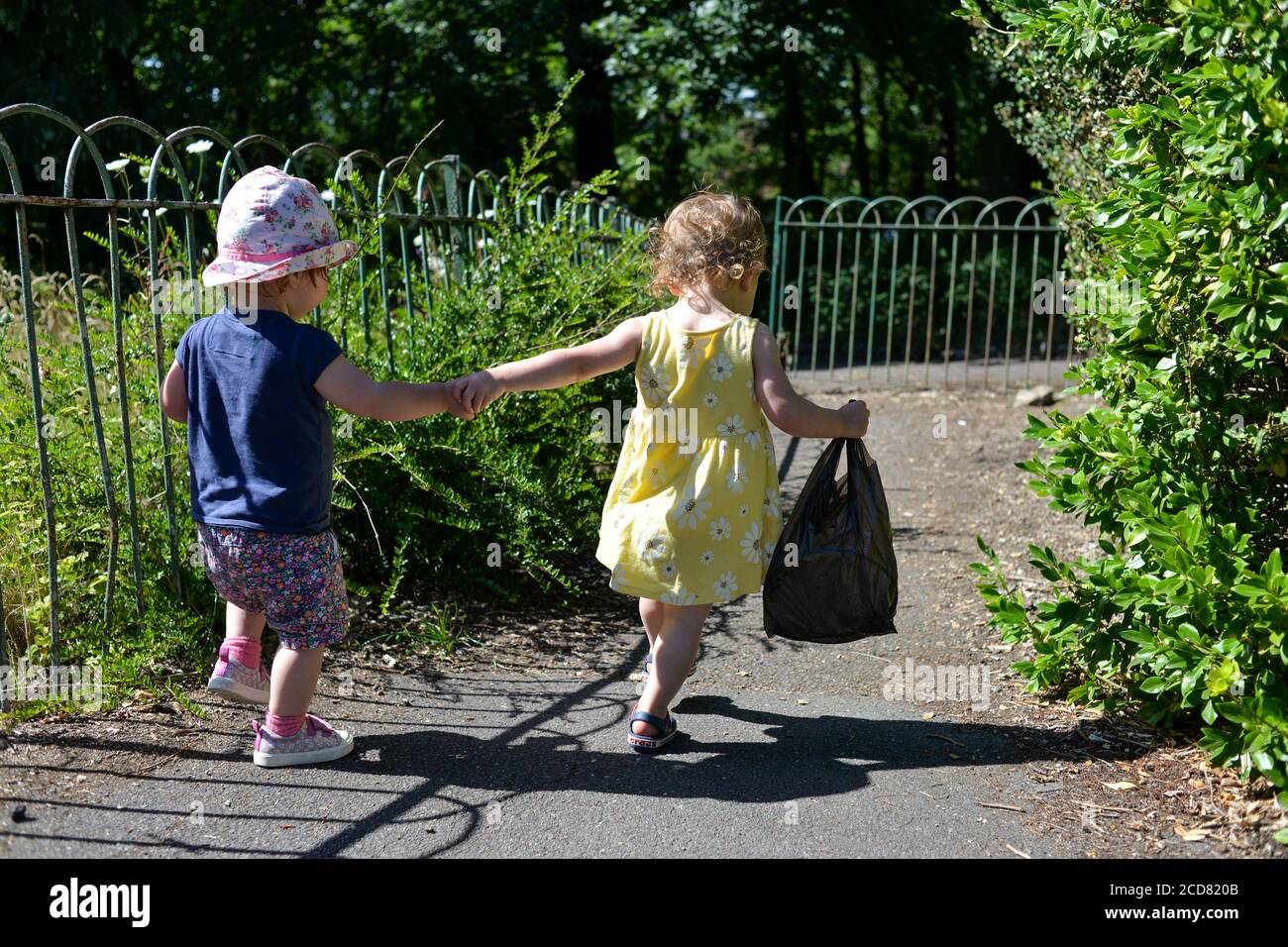 Zwei kleine Kinder halten sich die Hände und gehen einen Fußweg in Sommerkleidung und Sonnenschein Stockfoto