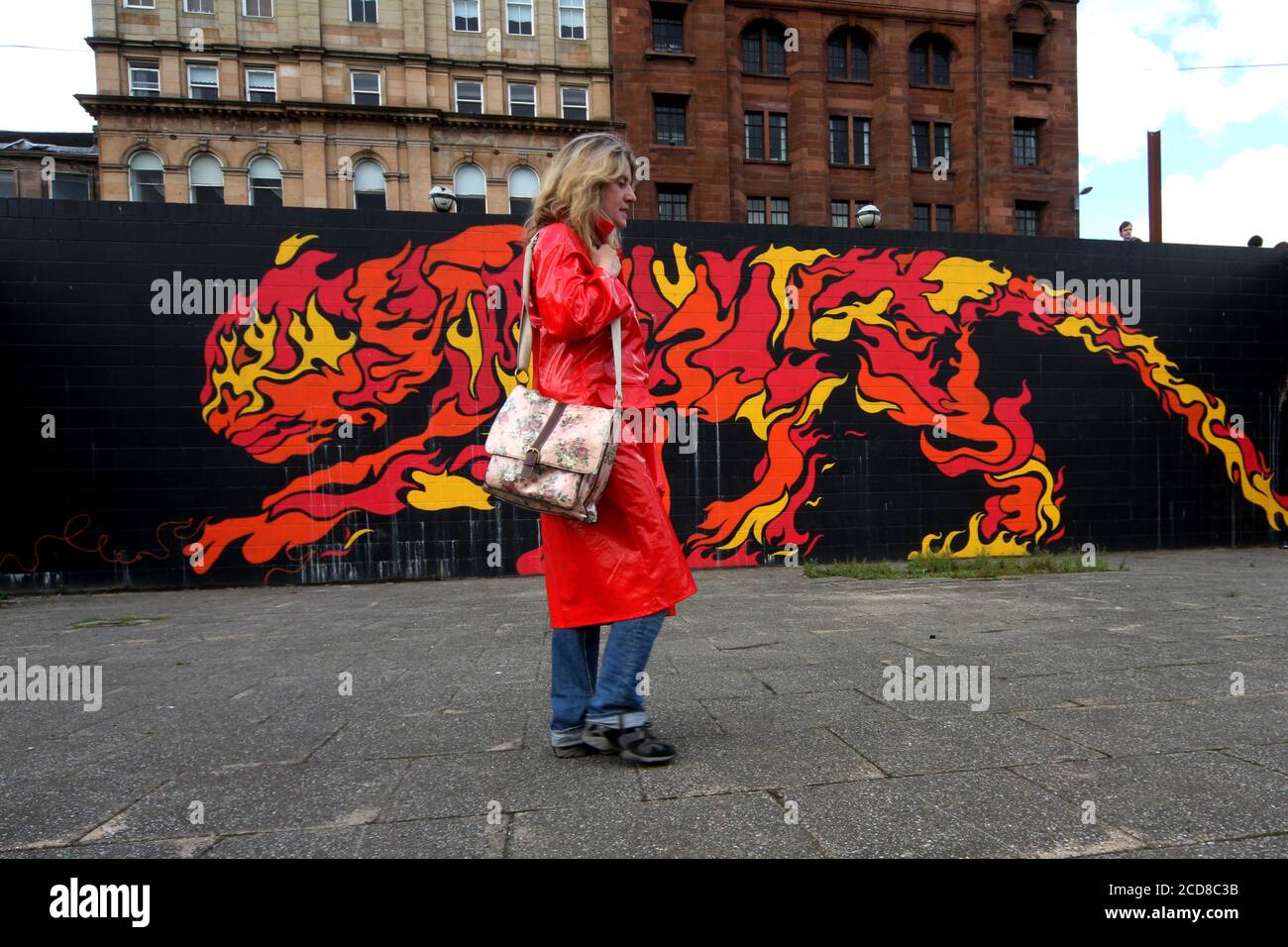 Glasgow, Schottland, Großbritannien. Frau in glänzendem roten Regenmantel sieht sich ein Wandgemälde an, das an der Wand des Flusses Clyde angebracht ist. Das Wandbild zeigt das chinesische Element des Feuers. Stockfoto