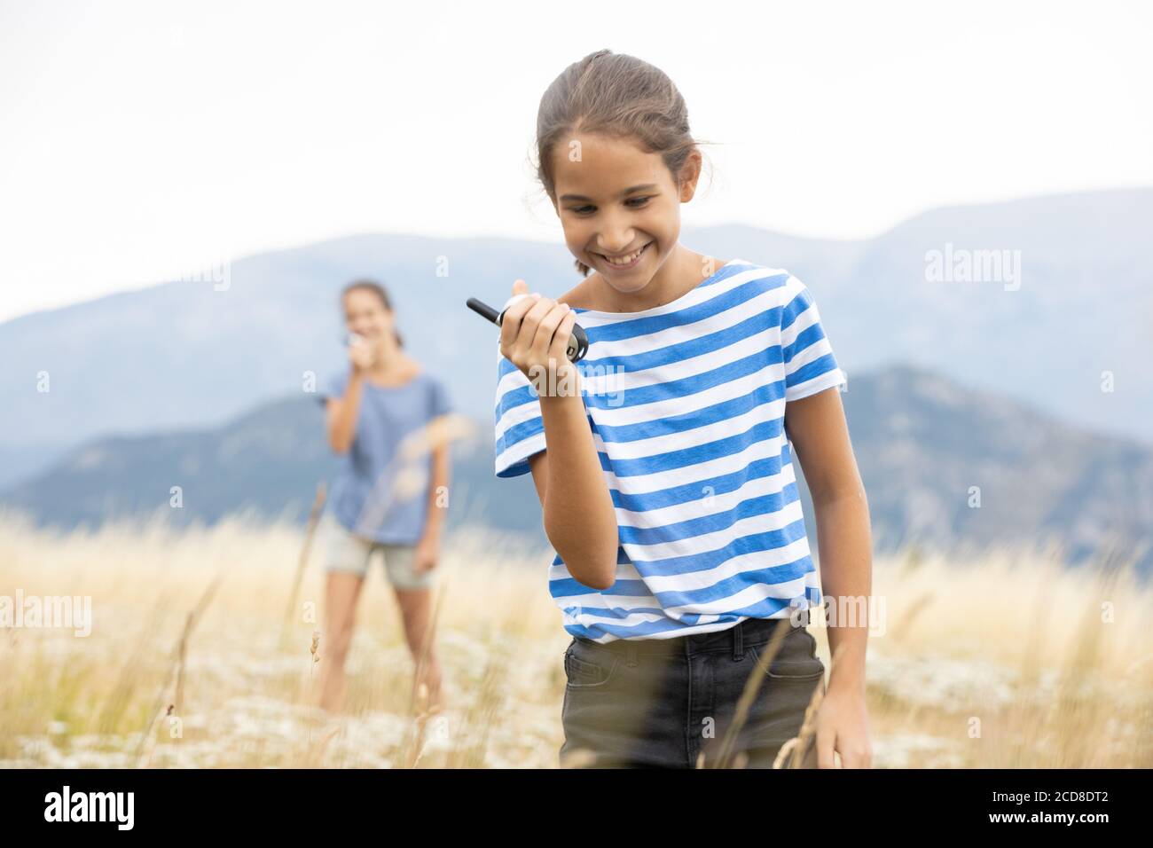 Mädchen im Walkie-Talkie, während ihre Schwester zuhört Sie im Hintergrund bei einem Familienspaziergang in der Wiese Stockfoto