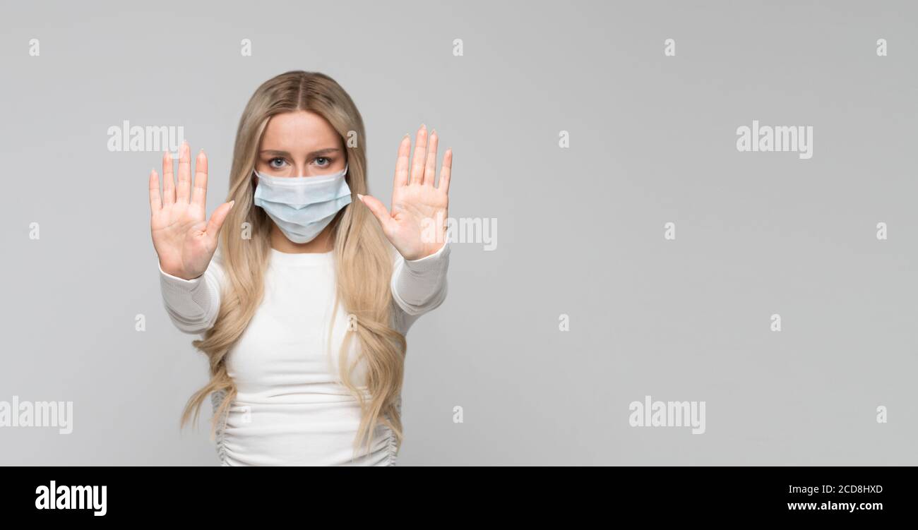 Grippe, covid-19 Saison. Nahaufnahme Studio Porträt von Frau in Schutzmaske halten die Hände in Stop-Geste, kopieren Raum, isoliert auf grauem Hintergrund Stockfoto