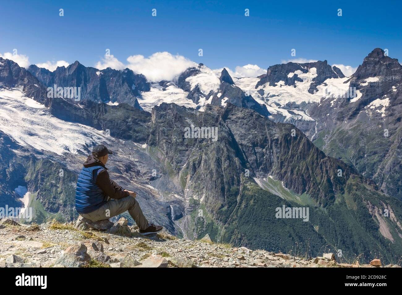 Mann am Rande des Abgrunds vor dem Hintergrund der Berggipfel im Schnee und blauen Himmel mit Wolken, Sommer sonnigen Tag Stockfoto