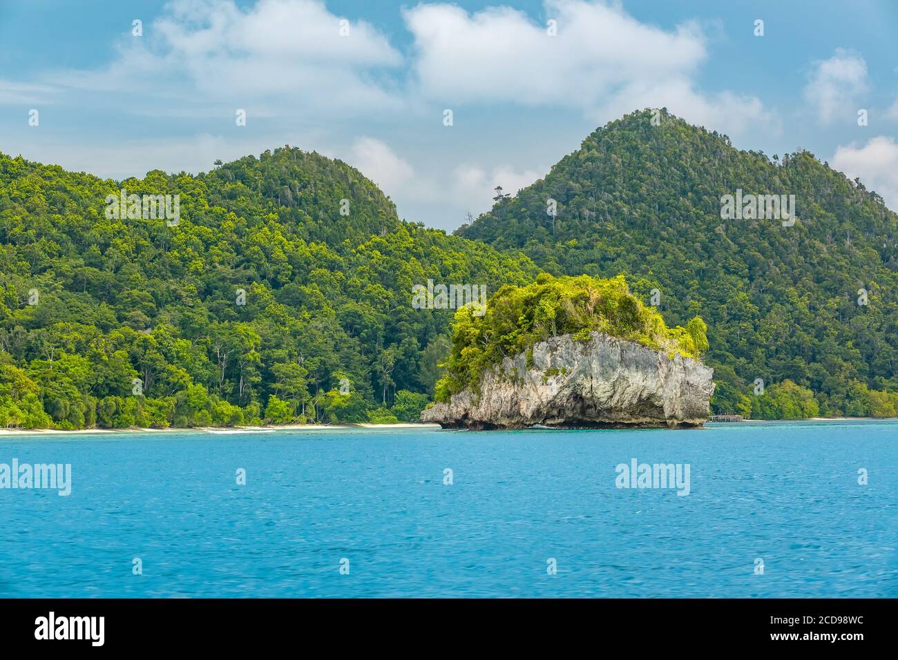Indonesien. Meerenge zwischen den Inseln. Tag. Küste mit Dschungel und kleine felsige Insel. Berge und Wolken am Horizont Stockfoto