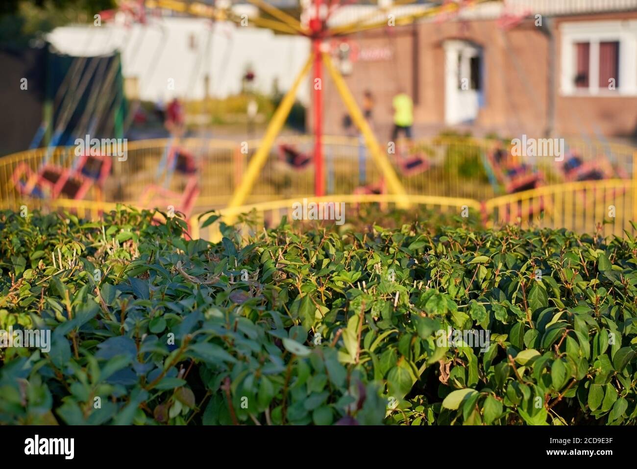 Kinderkettenkarussell in Bewegung unscharf, grüner Busch an einem Sommertag im Vordergrund. Stockfoto