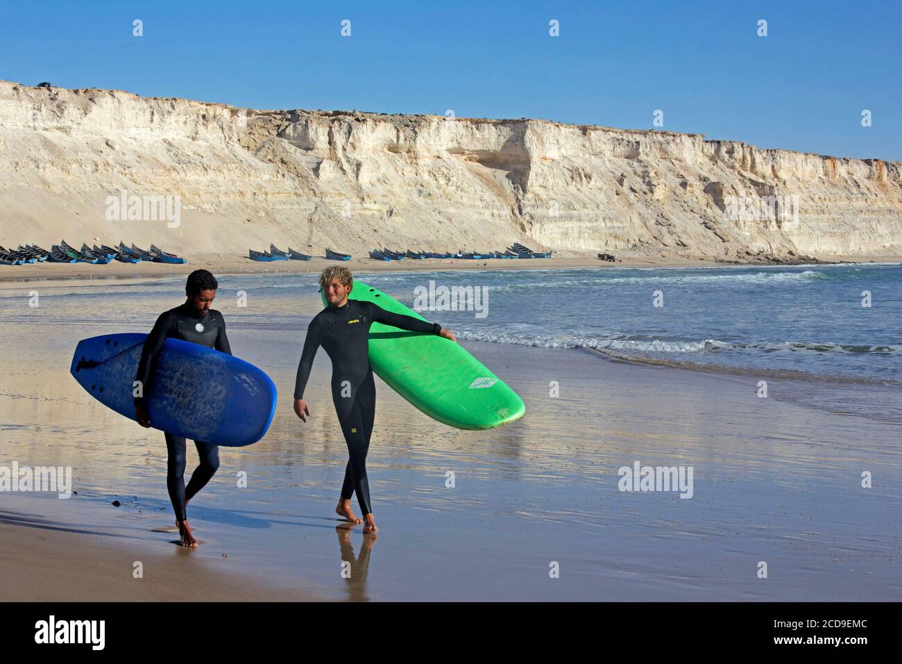 Marokko, Westsahara, Dakhla, zwei marokkanische Surfer mit ihren Brettern am Strand von Araiche, die von einer Klippe umgeben sind Stockfoto