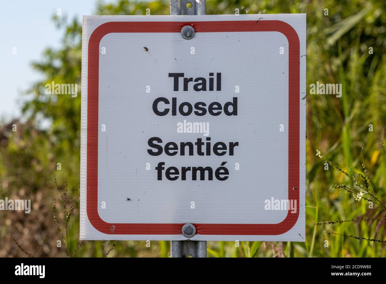 Weg geschlossen Zeichen in Englisch und Französisch mit überwucherten Weg Im Hintergrund Stockfoto