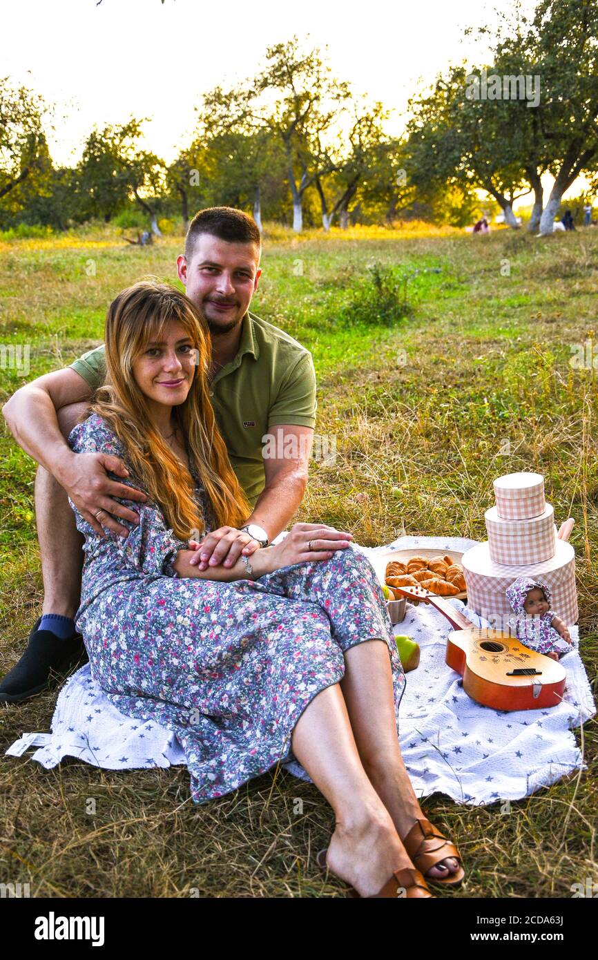 Glückliches junges Paar entspannend und mit Picknick im Park. Friedliche süße Pärchen genießen Abendessen im Park. Mann und Frau sitzen auf Gras und umarmen. Stockfoto