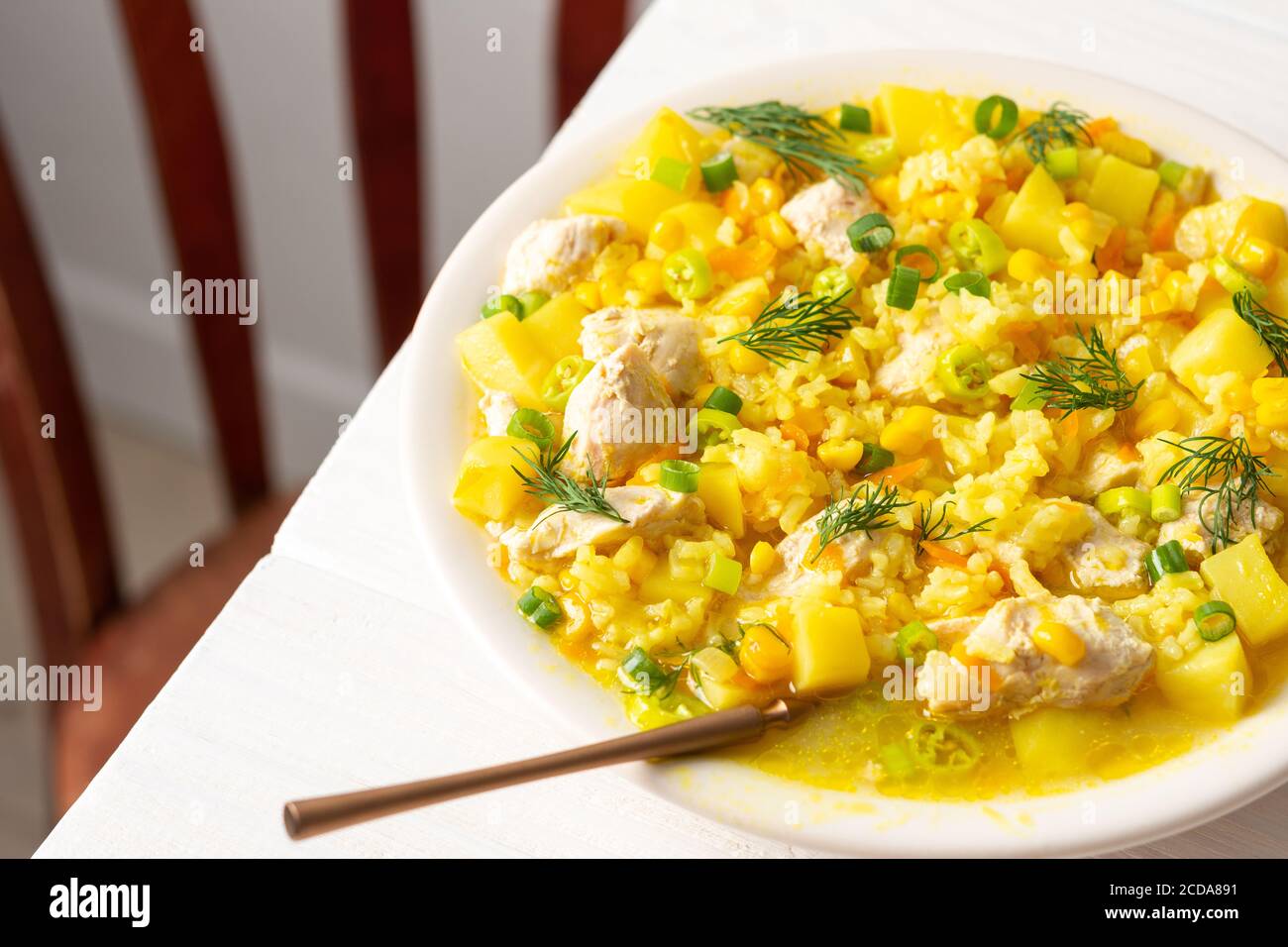 Leckeres herzhaftes Mittagessen, Suppe mit Huhn und Reis, jungen Mais, grüne Zwiebeln und Kartoffeln auf einem Teller auf dem Tisch Stockfoto