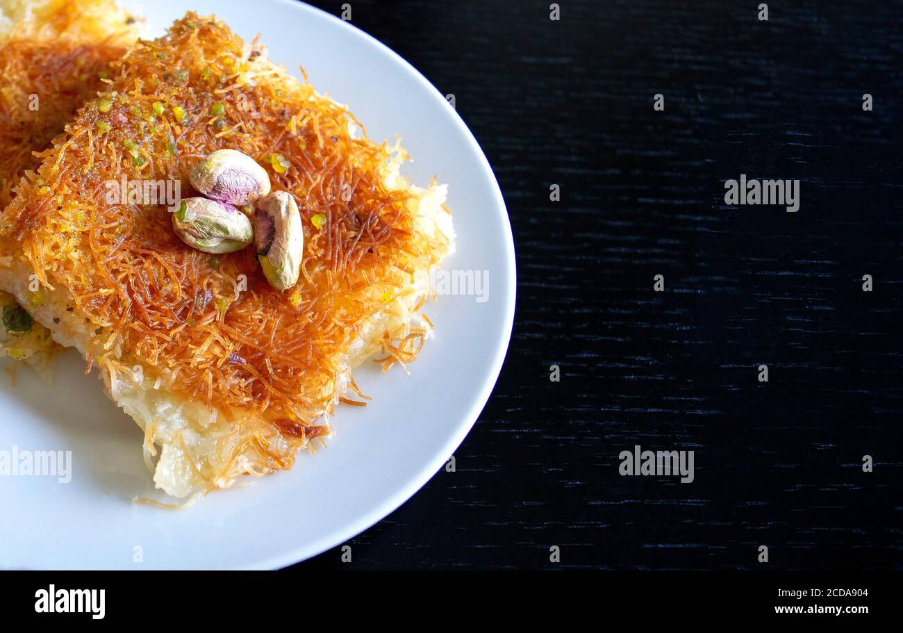 Traditionelle östliche Dessert Kunafa. Draufsicht. Arabischer Käse kunafa in weißer Platte auf dunklem Holztisch mit Kopierraum. Konafa. Stockfoto