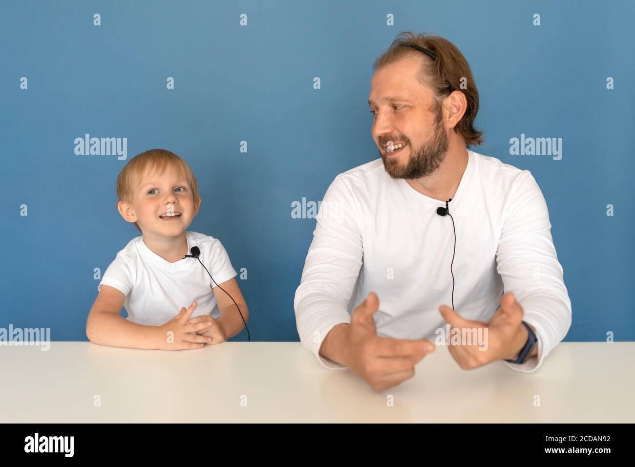 Zwei Personen, Vater und Sohn, ein Mann und ein Kind mit Mikrofonen auf weißen T-Shirts diskutieren etwas, Dreharbeiten ein Kinder-Video-Blog Unboxing für Yo Stockfoto