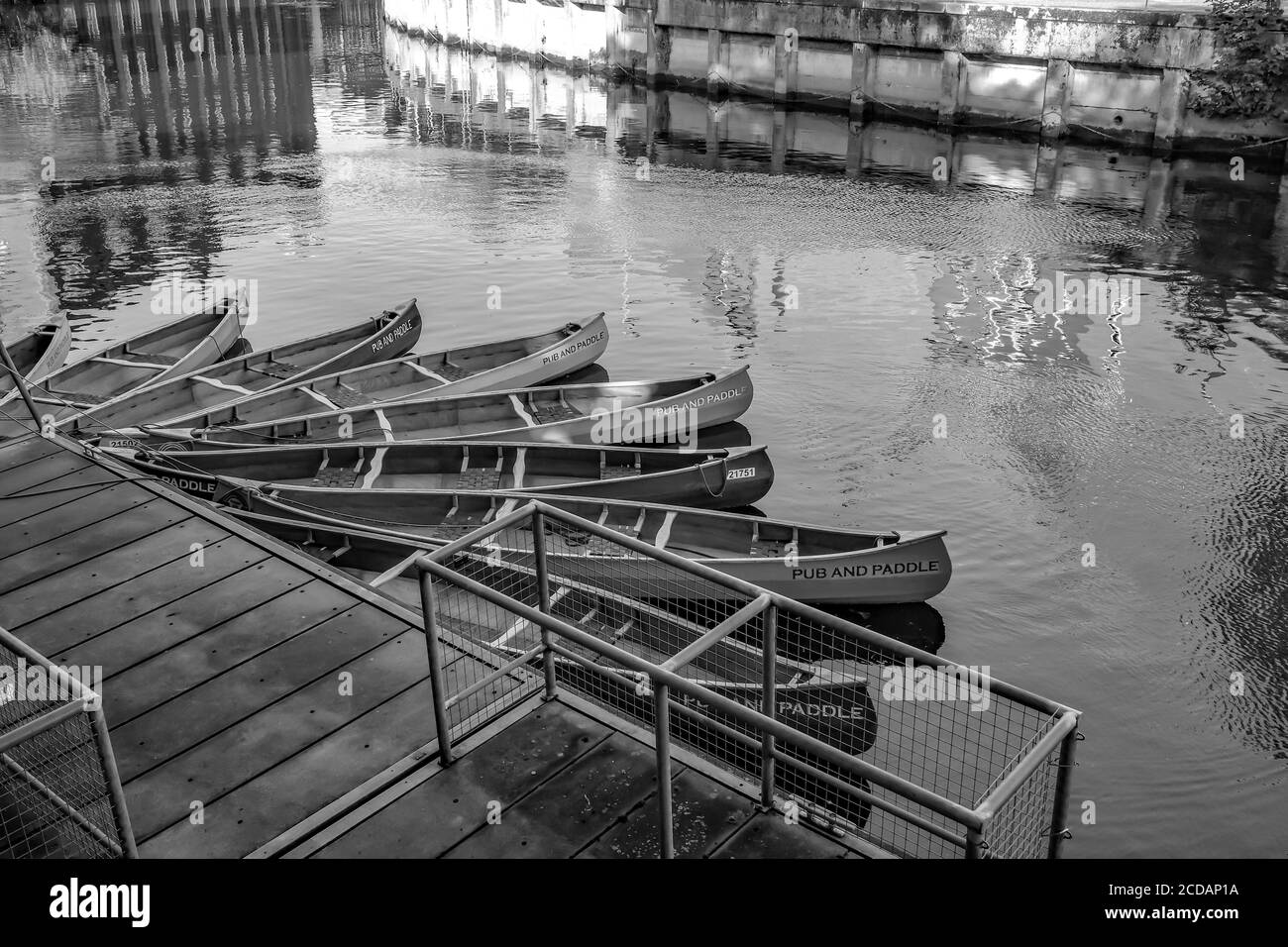 Ein Schwarz-Weiß-Foto der Kanus "Pub nad Paddle", die an Holzinszenierungen auf dem Fluss Wensum gebunden sind. Diese Kanus befinden sich in der Nähe des Ribs of Beef Pub und können für eine Kneipentour mit einem Unterschied gemietet werden. Es gibt viele Pubs am Fluss in Norwich und Sie können diese Kanus mieten, um sie zu besuchen. Stockfoto