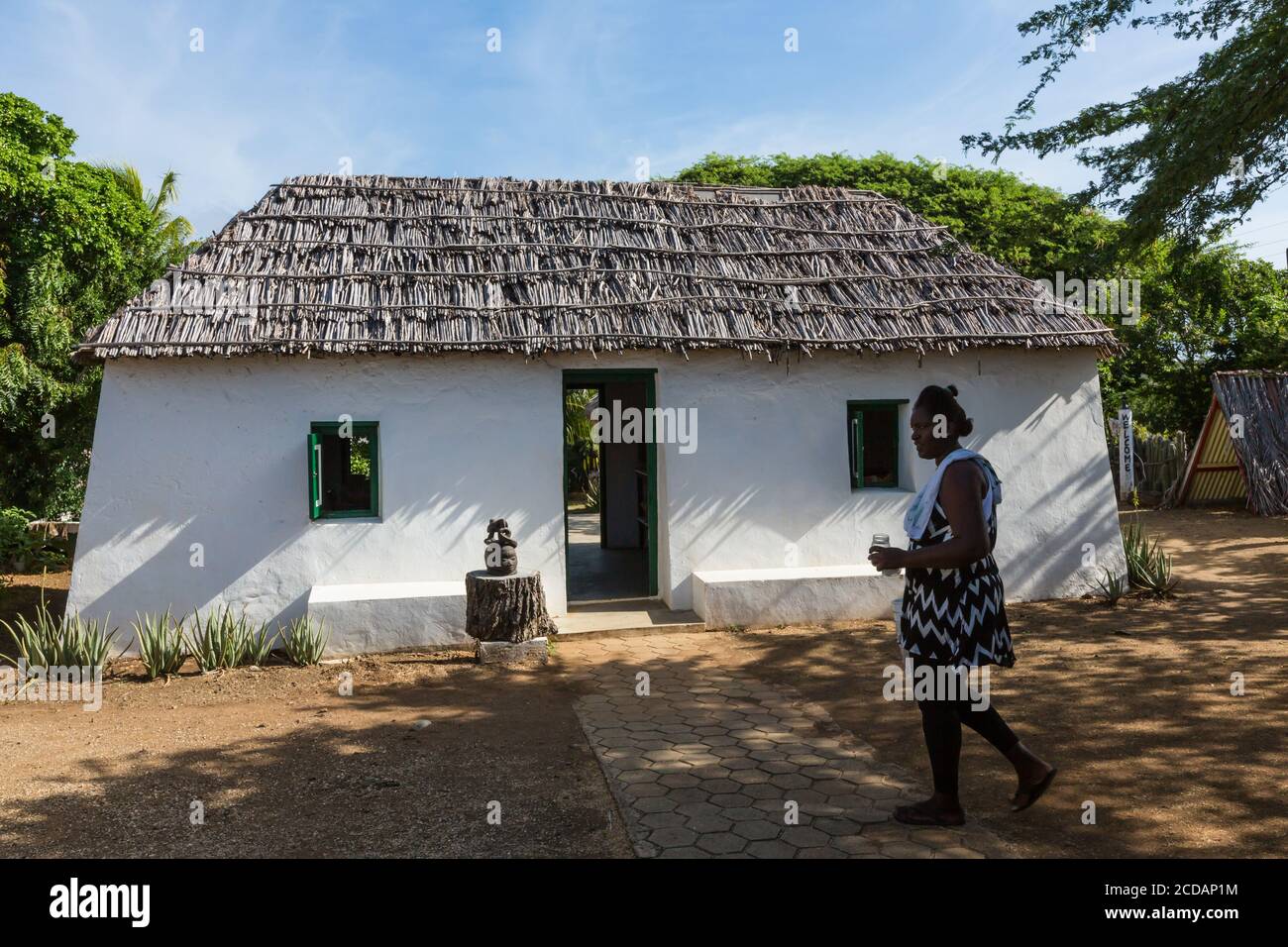 Eine Frau geht vor einem Kunuku-Haus, oder kas di pal’i maishi. Diese Häuser wurden ursprünglich als Häuser für die Sklaven auf den Plantagen auf Cu gebaut Stockfoto