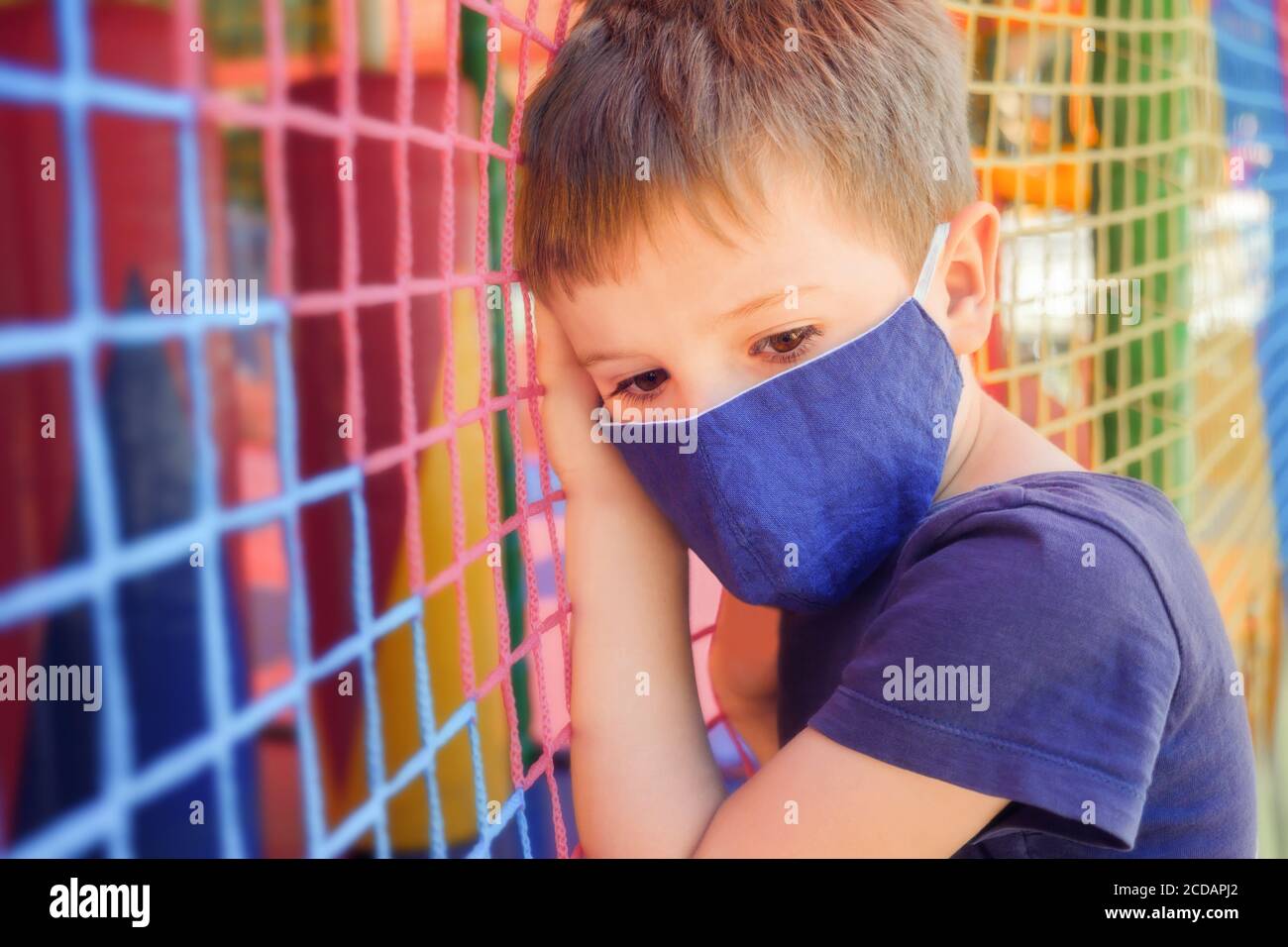 Junge in einer medizinischen Maske auf dem Spielplatz. Sicherheit Junge in Baumwolle Gesichtsmaske auf Spielplatz Hintergrund. Das Konzept des Schutzes gegen Coronavirus Stockfoto