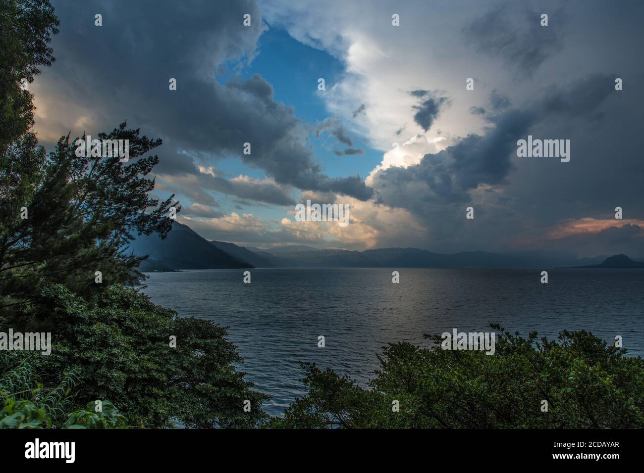 Stürmische Wolken über dem Atitlan See in Guatemala bei Sonnenuntergang. Der See ist eine riesige Caldera oder Vulkankrater, gefüllt mit Wasser. Stockfoto