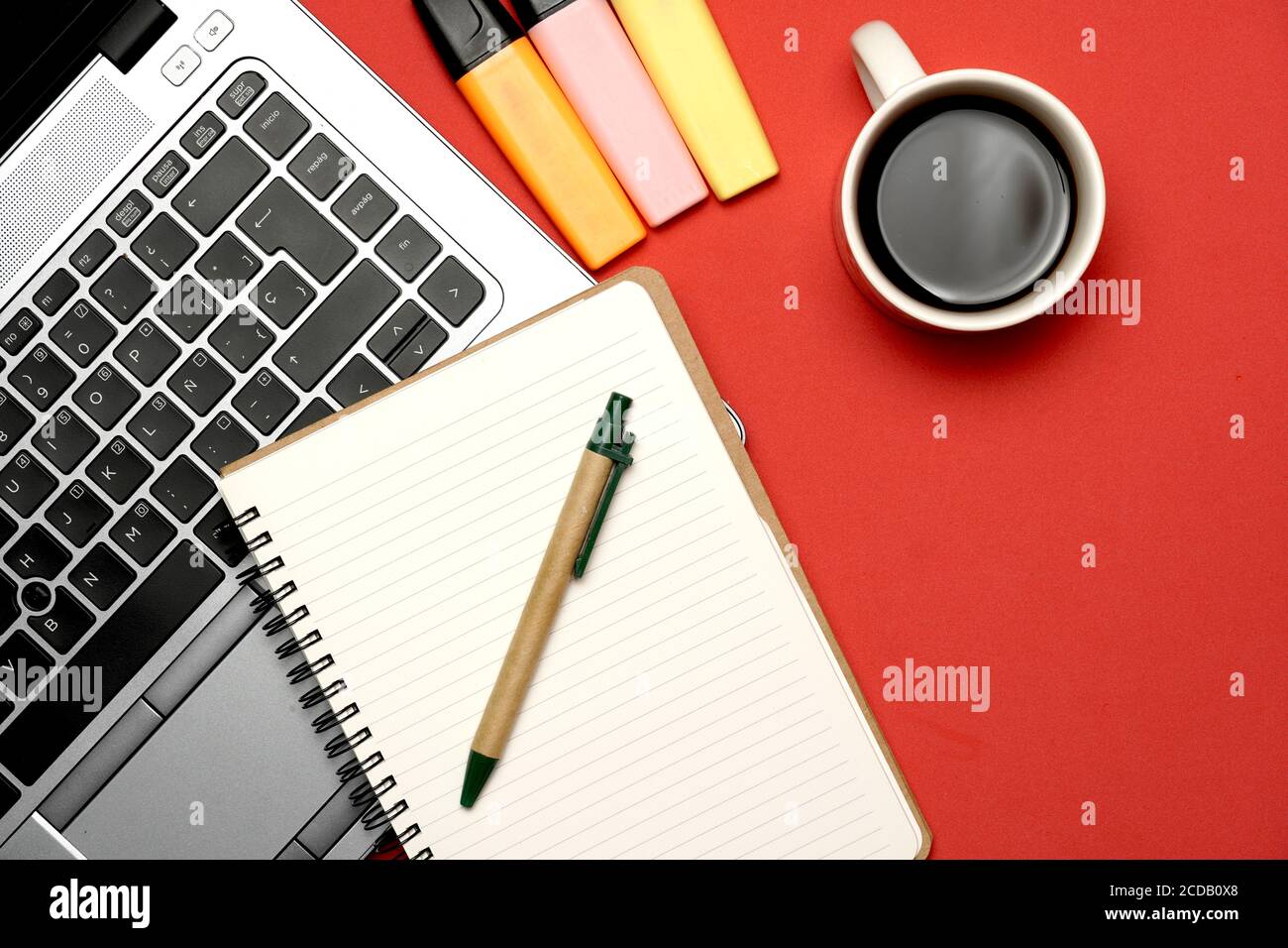 Draufsicht des Arbeitsbereichs auf einem roten Hintergrund mit Laptop braun farbigen Markierungen Notebook und Stift. Flach liegend flach in Form Stockfoto