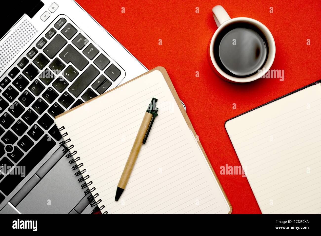 Draufsicht des Arbeitsbereichs auf rotem Hintergrund mit Laptop-braunem Notebook-Kaffee und Stift. Flach liegend flach in Form Stockfoto