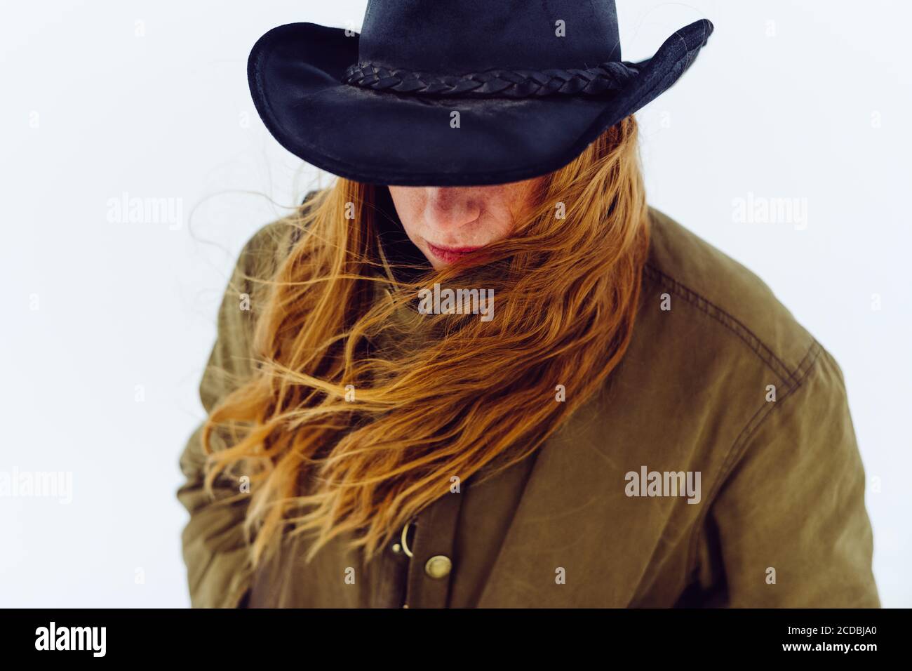 Selbstbewusste westliche Frau mit Cowboyhut geht mit Kamera und im Wind fließendem Haar um den Schnee. Stockfoto