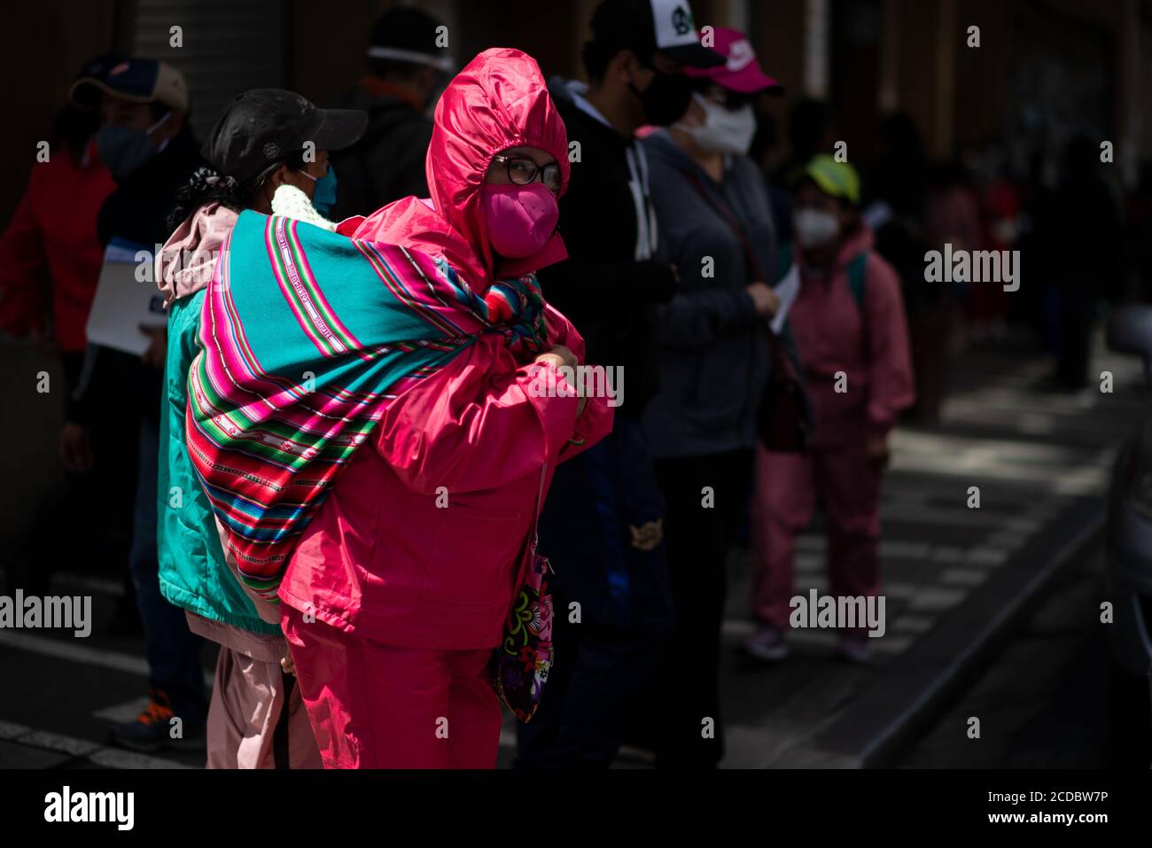 La Paz, Bolivien. August 2020. Eine Frau, die einen Biosicherheitsanzug und  eine traditionelle aguayo Decke trägt, die als Rucksack verwendet wird,  überquert eine Straße Stockfotografie - Alamy