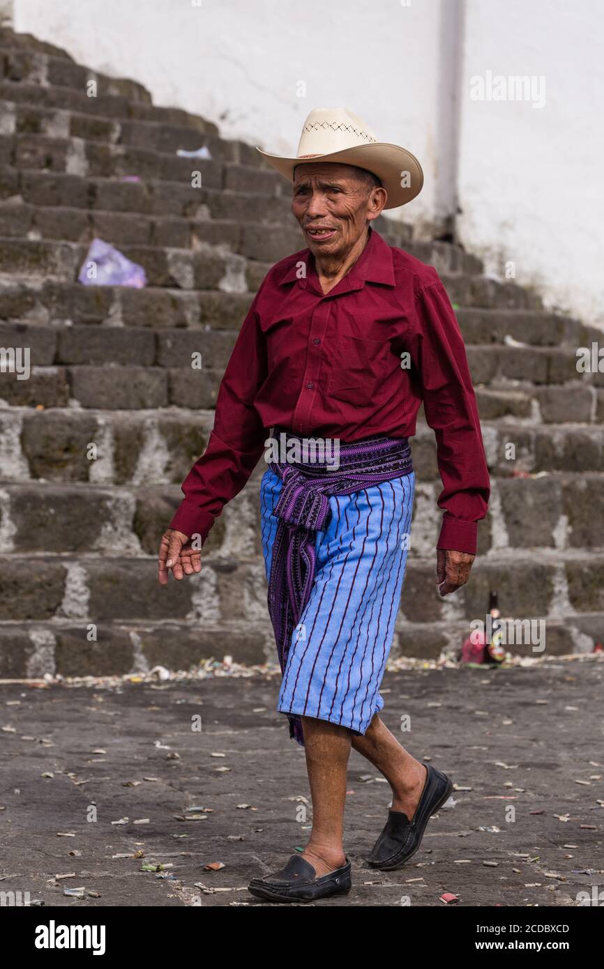 Ein Tzutujil Maya Mann in traditioneller Kleidung geht vor den Stufen der Kirche von Santiago in Santiago Atitlan, Guatemala. Stockfoto