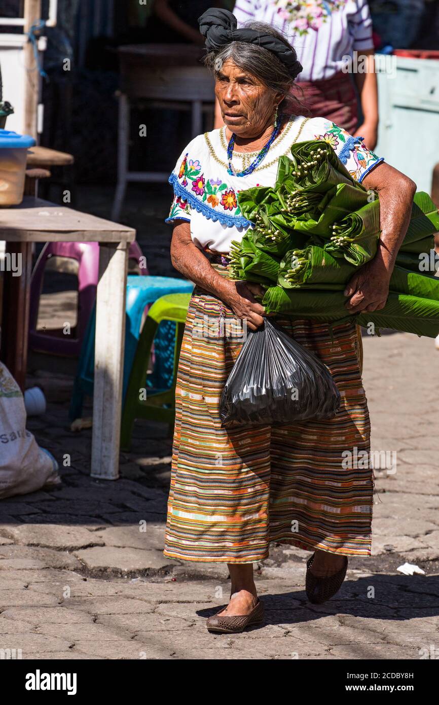 Eine ältere Tzutujil Maya Frau in traditioneller Kleidung trägt Bündel von Bananenblättern auf dem wöchentlichen offenen Markt in Santiago Atitlan, Guatemala. Stockfoto