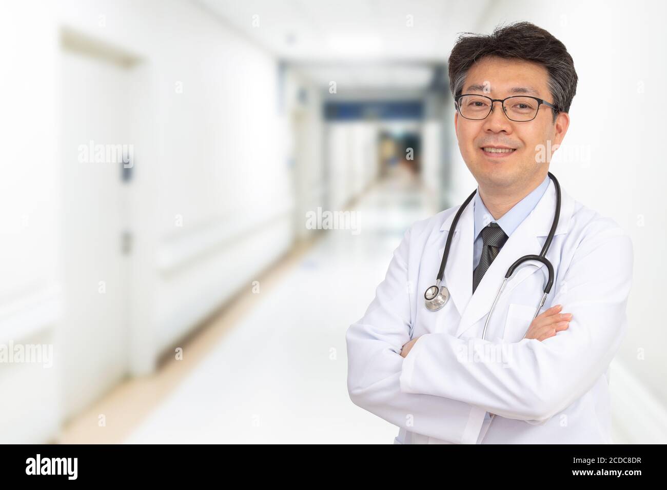 Ein asiatischer Arzt mittleren Alters lächelt im Krankenhausflur. Stockfoto