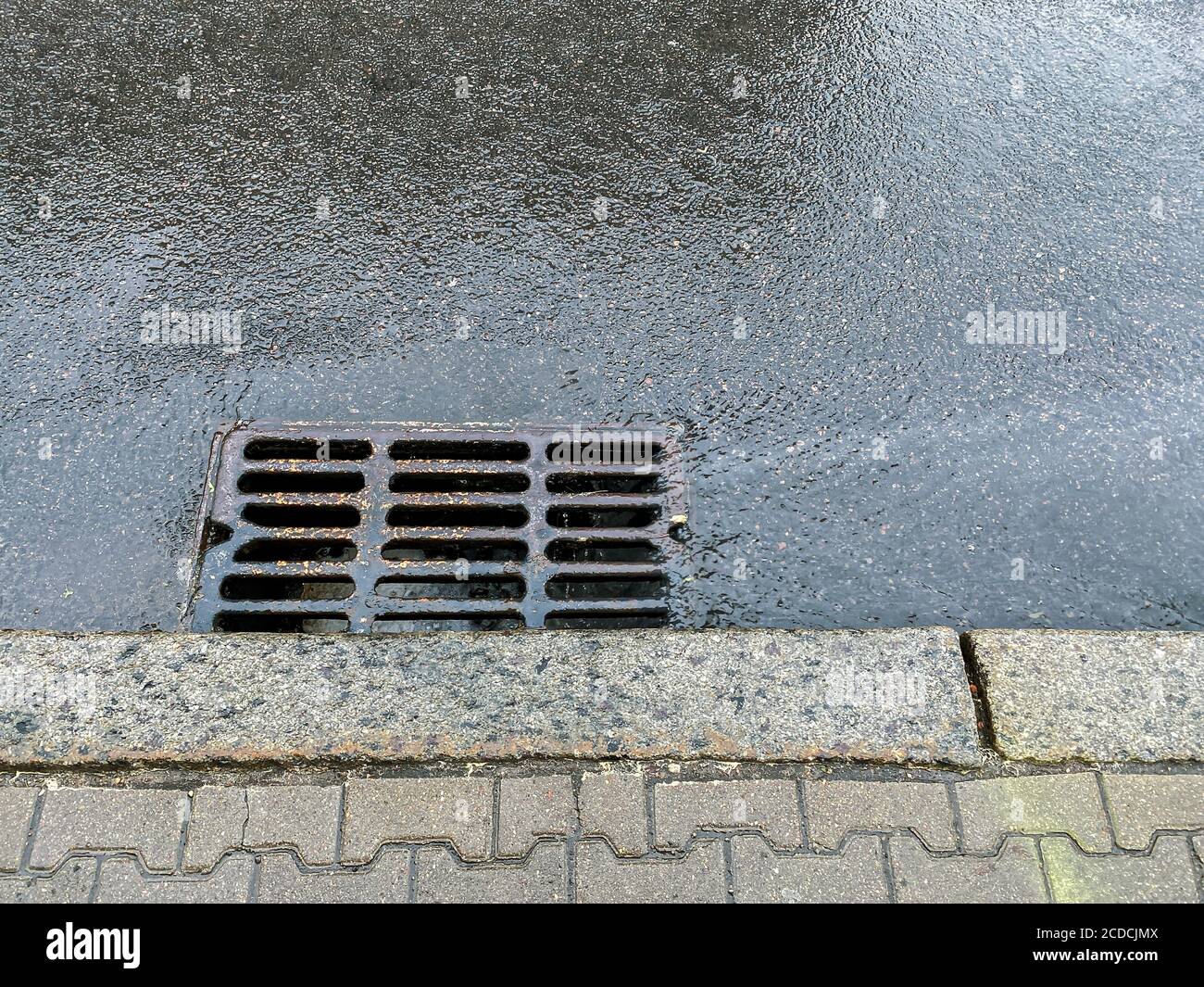Metall-Sturmabfluss auf der Straße. Regenwasser aus heftigem Regen fließt in einen Sturmabfluss Stockfoto