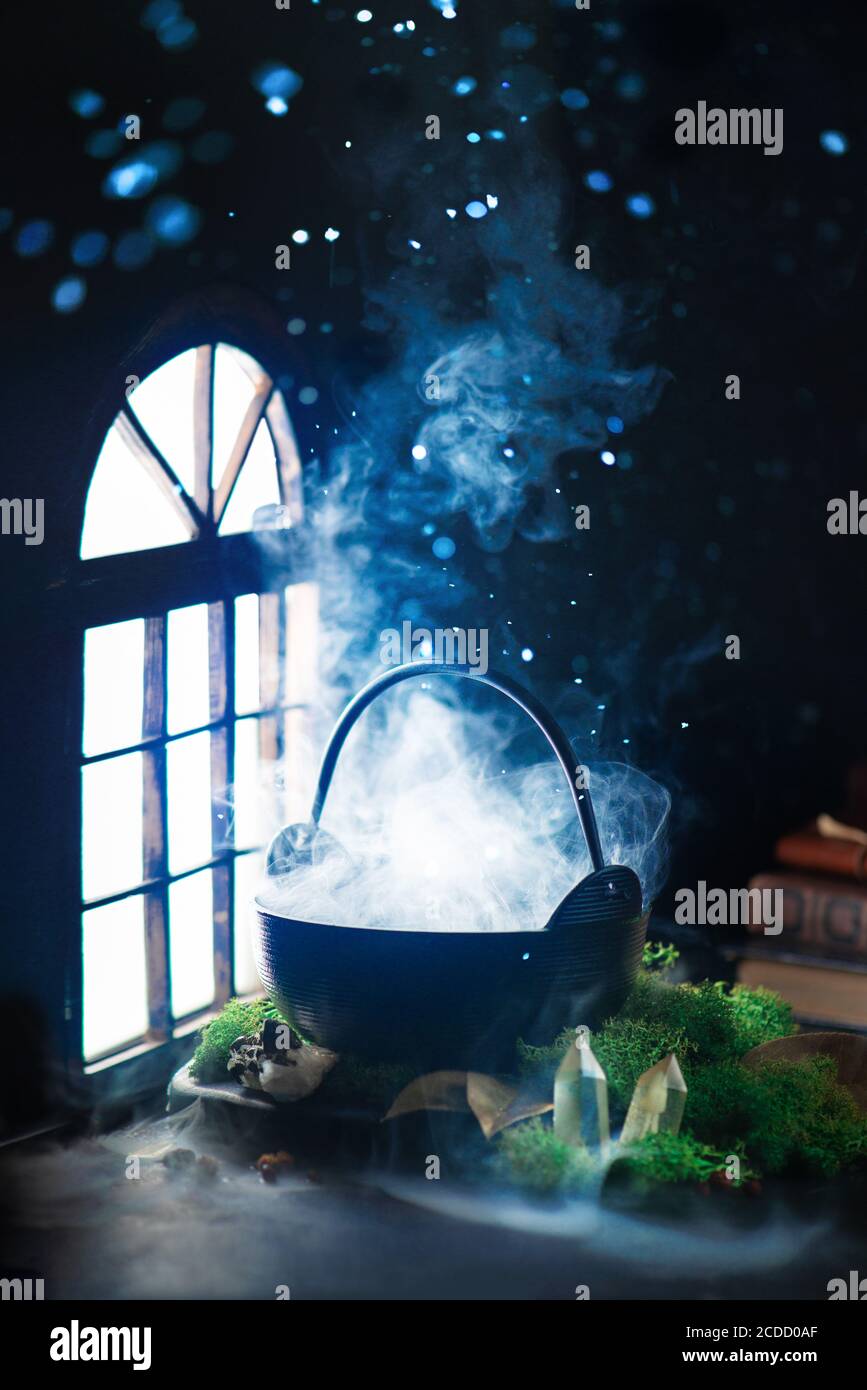 Kessel mit dichtem Dampf in der Nähe eines glänzenden Fensters, Hexenarbeitsplatz, magisches Stillleben Stockfoto