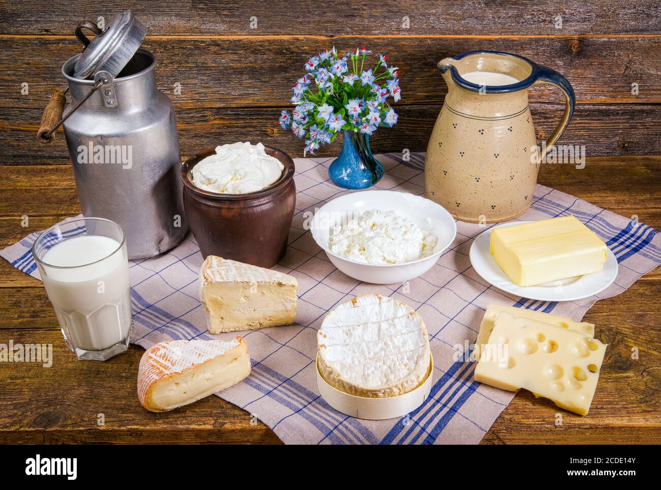 Milch in einem Krug und einem Glas, verschiedene Käsesorten, Schlagsahne, Quark und ein Stück Butter in einer rustikalen Landschaft auf einem Holztisch mit Küche Stockfoto