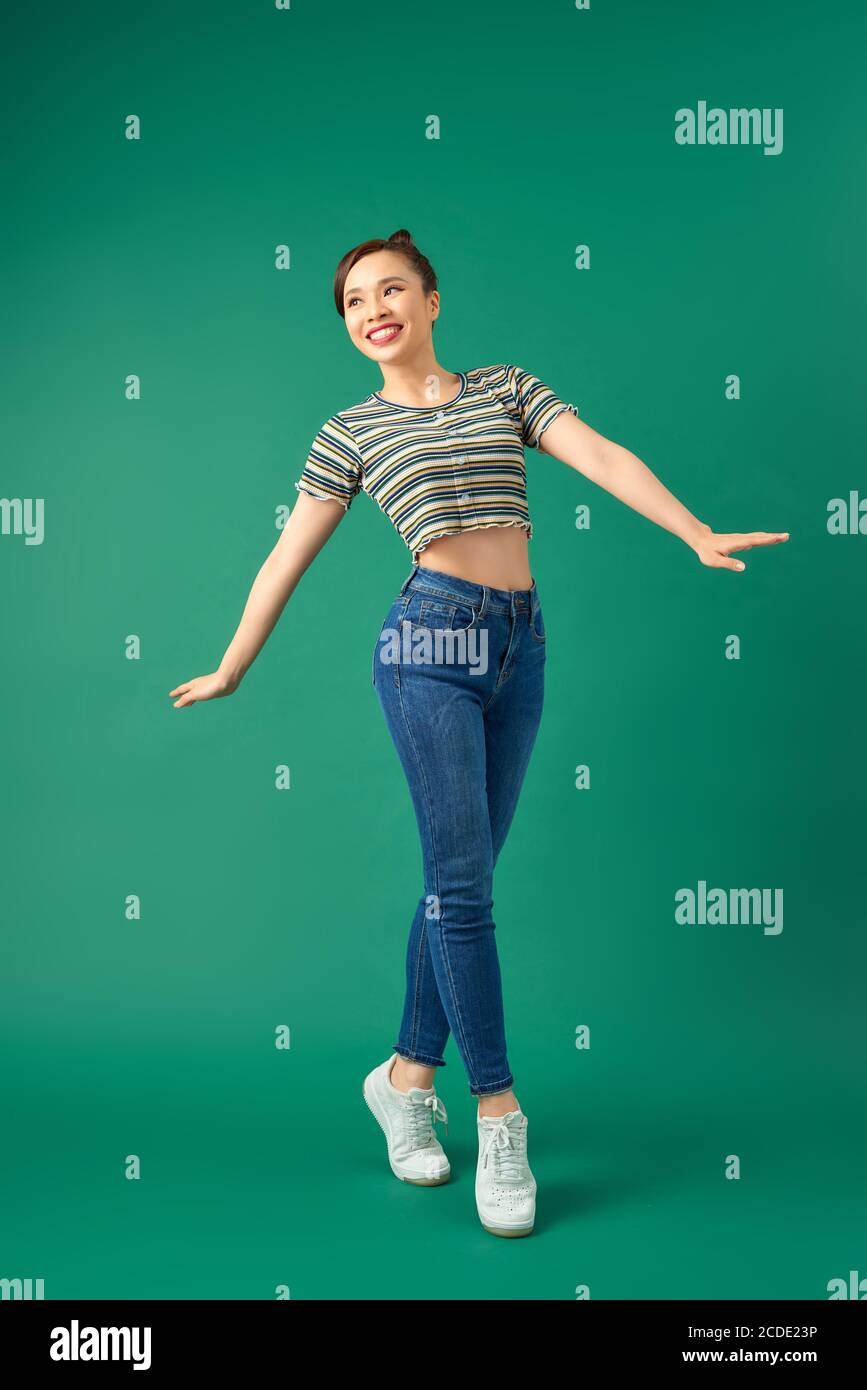 Fröhliche junge asiatische Frau auf einem Bein stehen. Volle Länge Ansicht der glückseligen Mädchen tanzen auf grünem Hintergrund. Stockfoto