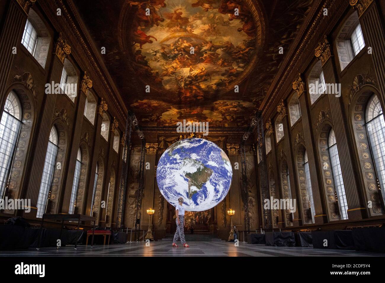 Ein Mitarbeiter betrachtet Luke Jerrams Kunstwerk Gaia, eine Nachbildung des Planeten Erde, die mit detaillierten NASA-Bildern der Erdoberfläche erstellt wurde, wie es im Rahmen des Greenwich+Docklands International Festival 2020 in der Painted Hall des Old Royal Naval College in Greenwich, London, gezeigt wird. Stockfoto