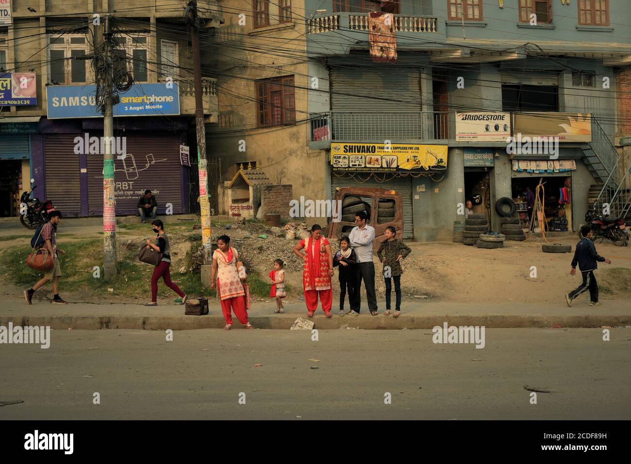 Fußgänger gehen, während eine Familie auf öffentliche Verkehrsmittel auf der Seite der Straße zwischen Kathmandu und Dhulikhel, Nepal wartet. Stockfoto