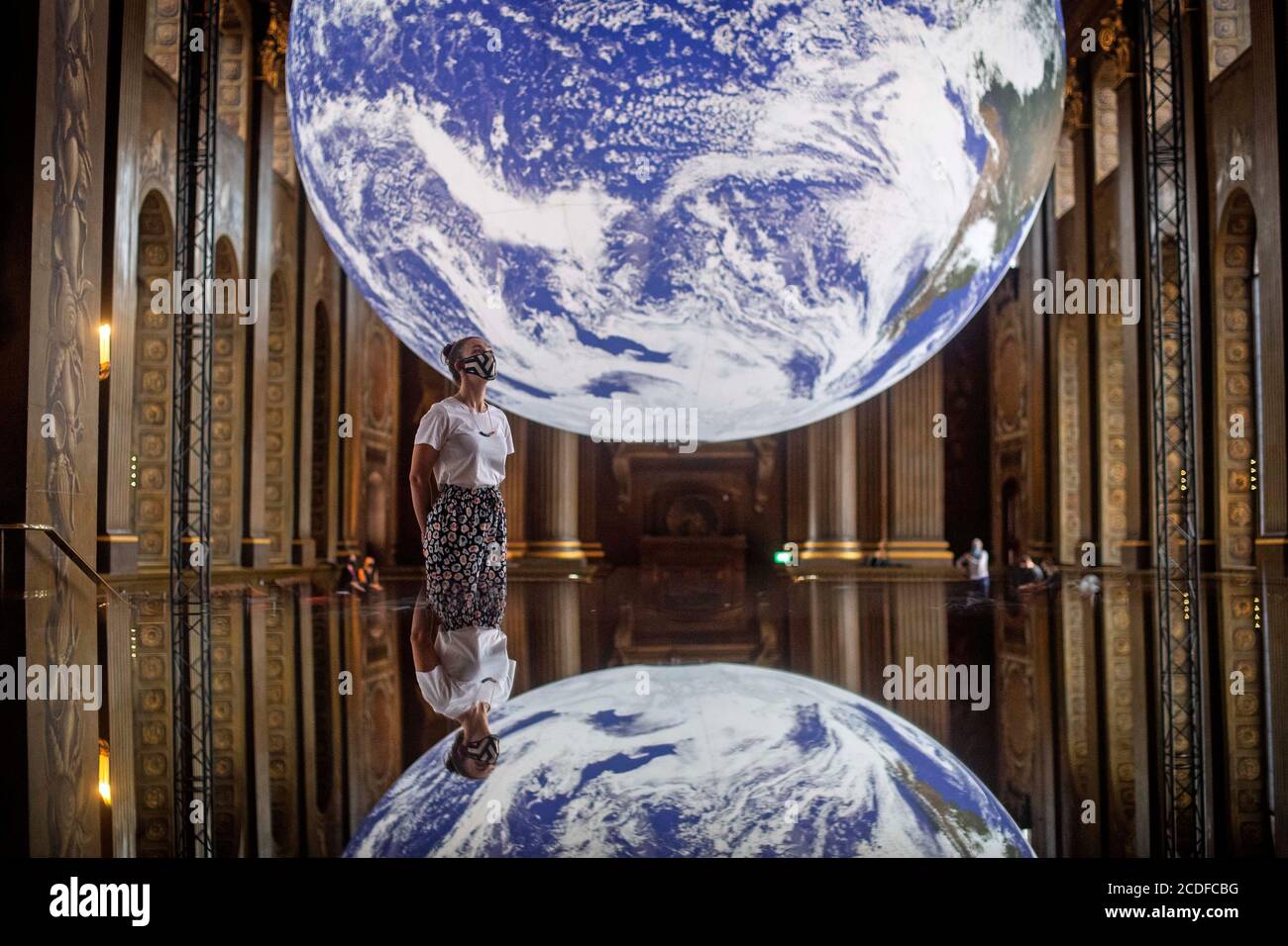 Ein Mitarbeiter betrachtet Luke Jerrams Kunstwerk Gaia, eine Nachbildung des Planeten Erde, die mit detaillierten NASA-Bildern der Erdoberfläche erstellt wurde, wie es im Rahmen des Greenwich+Docklands International Festival 2020 in der Painted Hall des Old Royal Naval College in Greenwich, London, gezeigt wird. Stockfoto