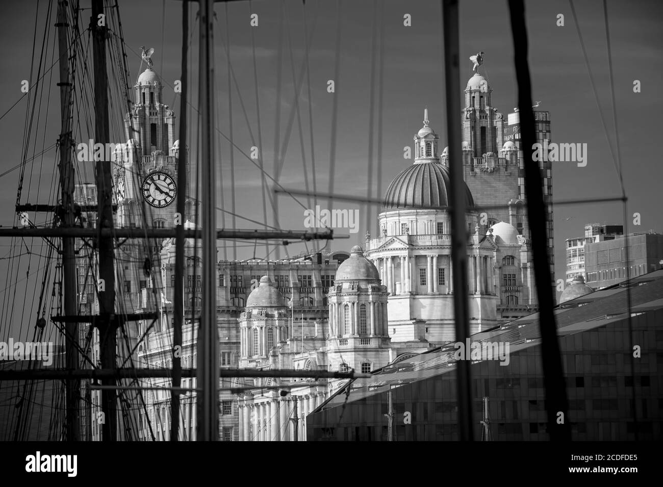 Blick durch entkochte Takelage und Masten von Schiffen zu ikonischen großen alten Gebäuden am Wasser, den drei Graces, von Liverpool, Großbritannien. Selektiver Fokus auf Bui Stockfoto