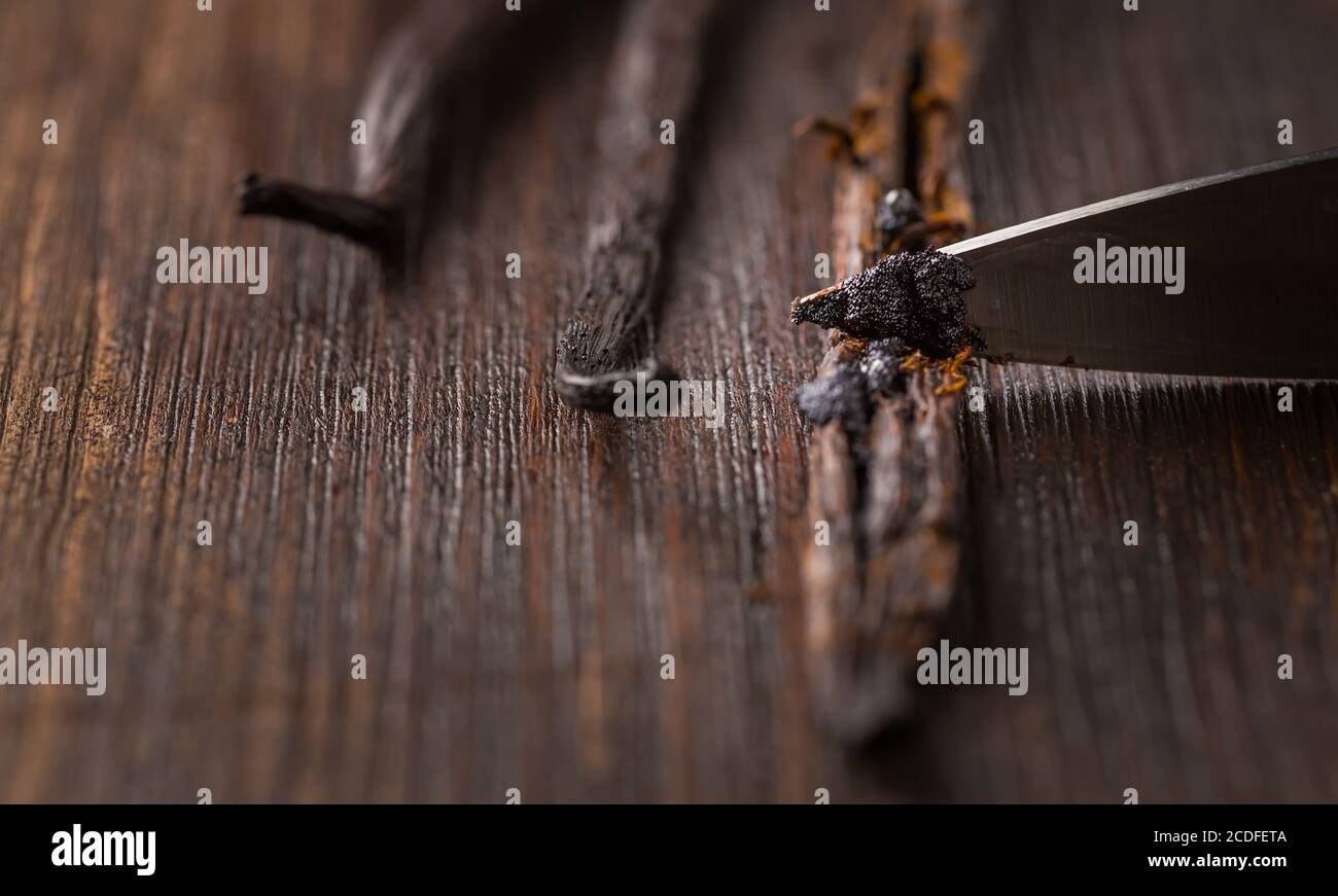 Vanilleschoten und Samenschoten mit Messer auf Holzhintergrund. Zubereitung von Vanille als Backzutat. Stockfoto