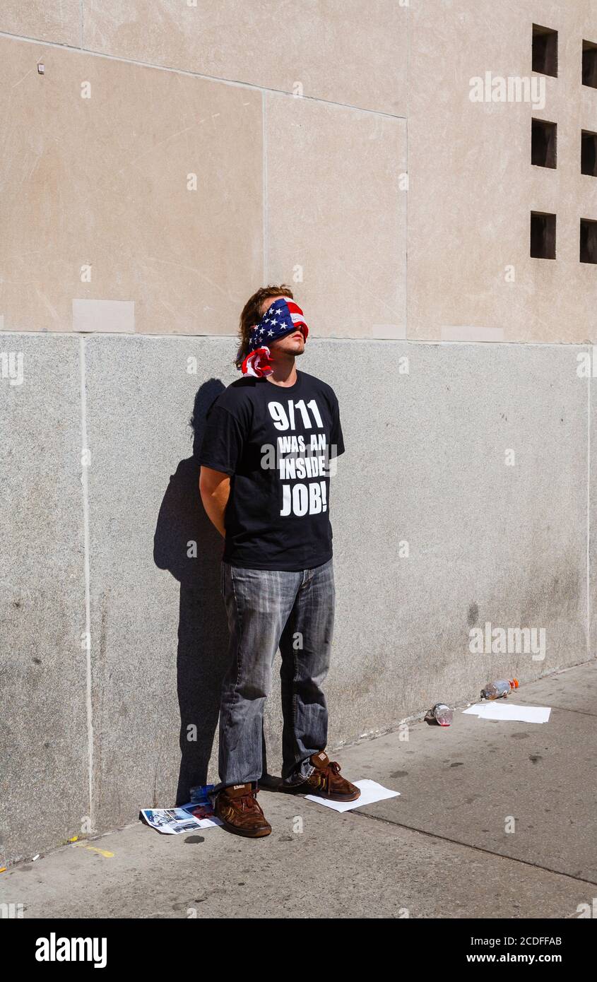 Ein junger amerikanischer Mann steht mit verbundenen Augen am World Trade Center in New York und trägt ein schwarzes T-Shirt mit der Aufschrift: "9/11 war ein Innenjob!" Stockfoto