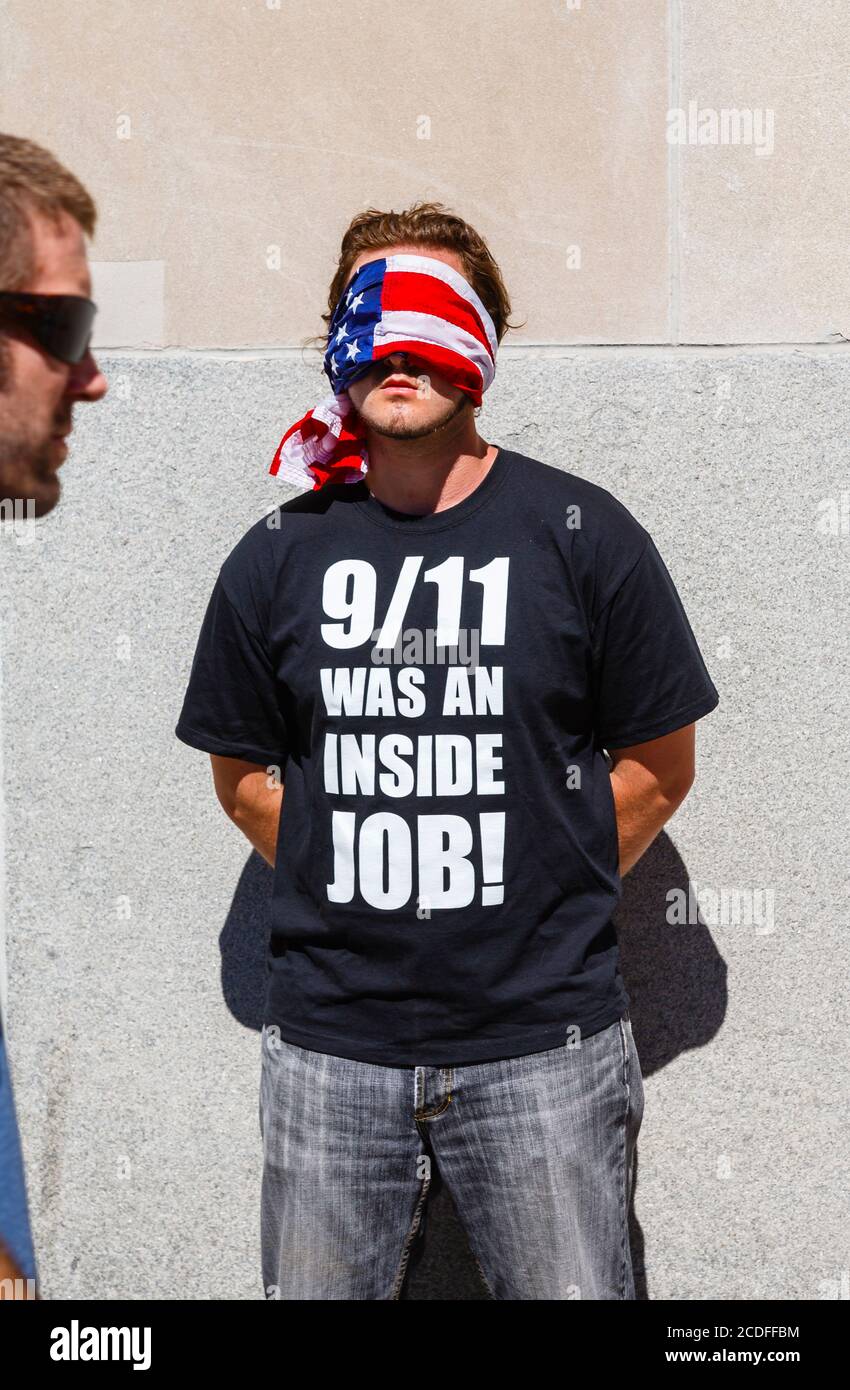 Ein junger amerikanischer Mann steht mit verbundenen Augen am World Trade Center in New York und trägt ein schwarzes T-Shirt mit der Aufschrift: "9/11 war ein Innenjob!" Stockfoto