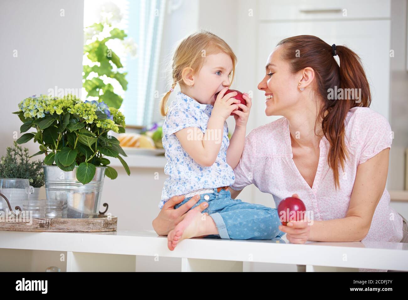 Mutter und Tochter essen jeweils einen Apfel in der Küche Stockfoto