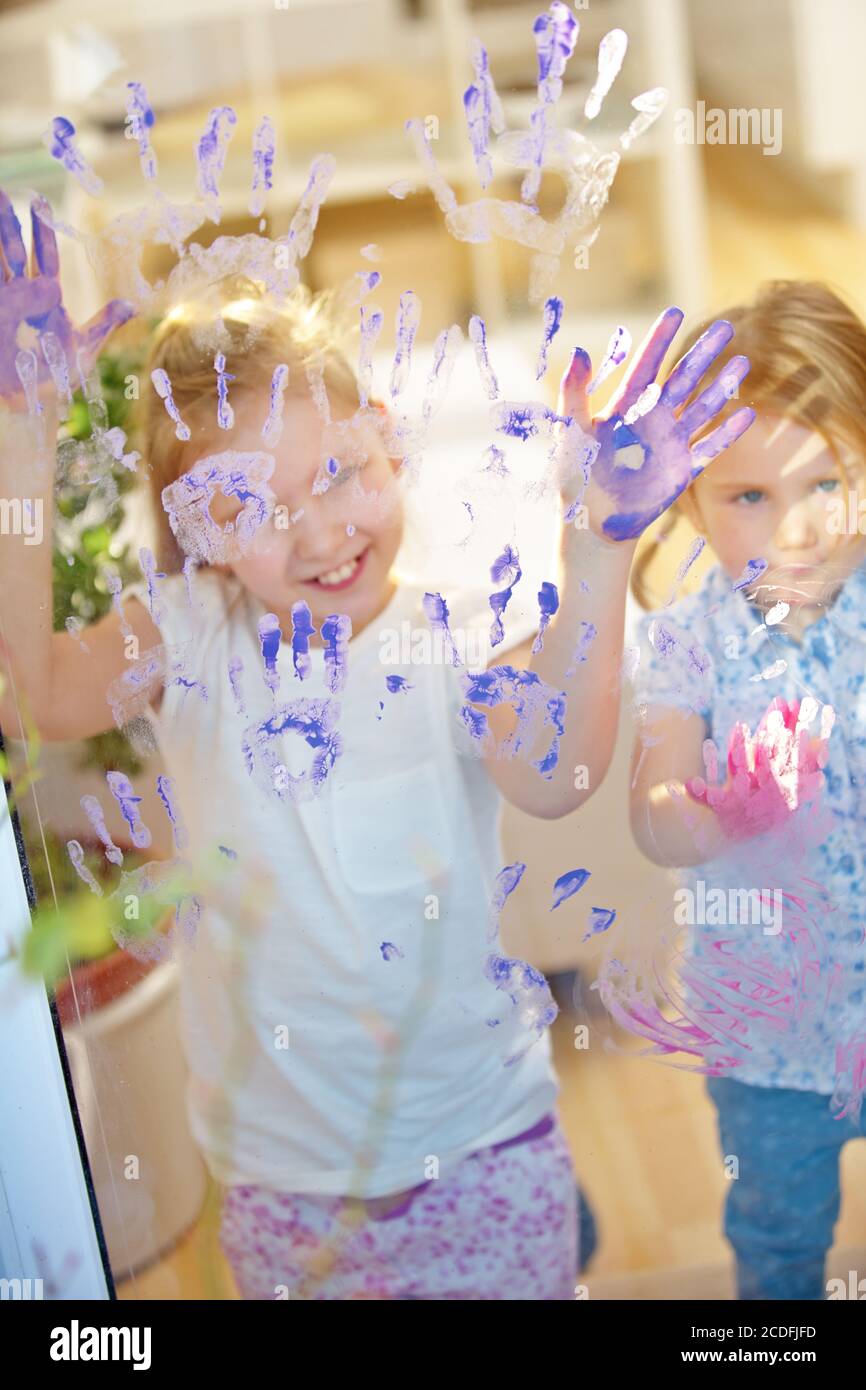 Kinder verwenden Fingerfarbe, um ihre Hände auf einem zu malen Glasscheibe im Kindergarten Stockfoto