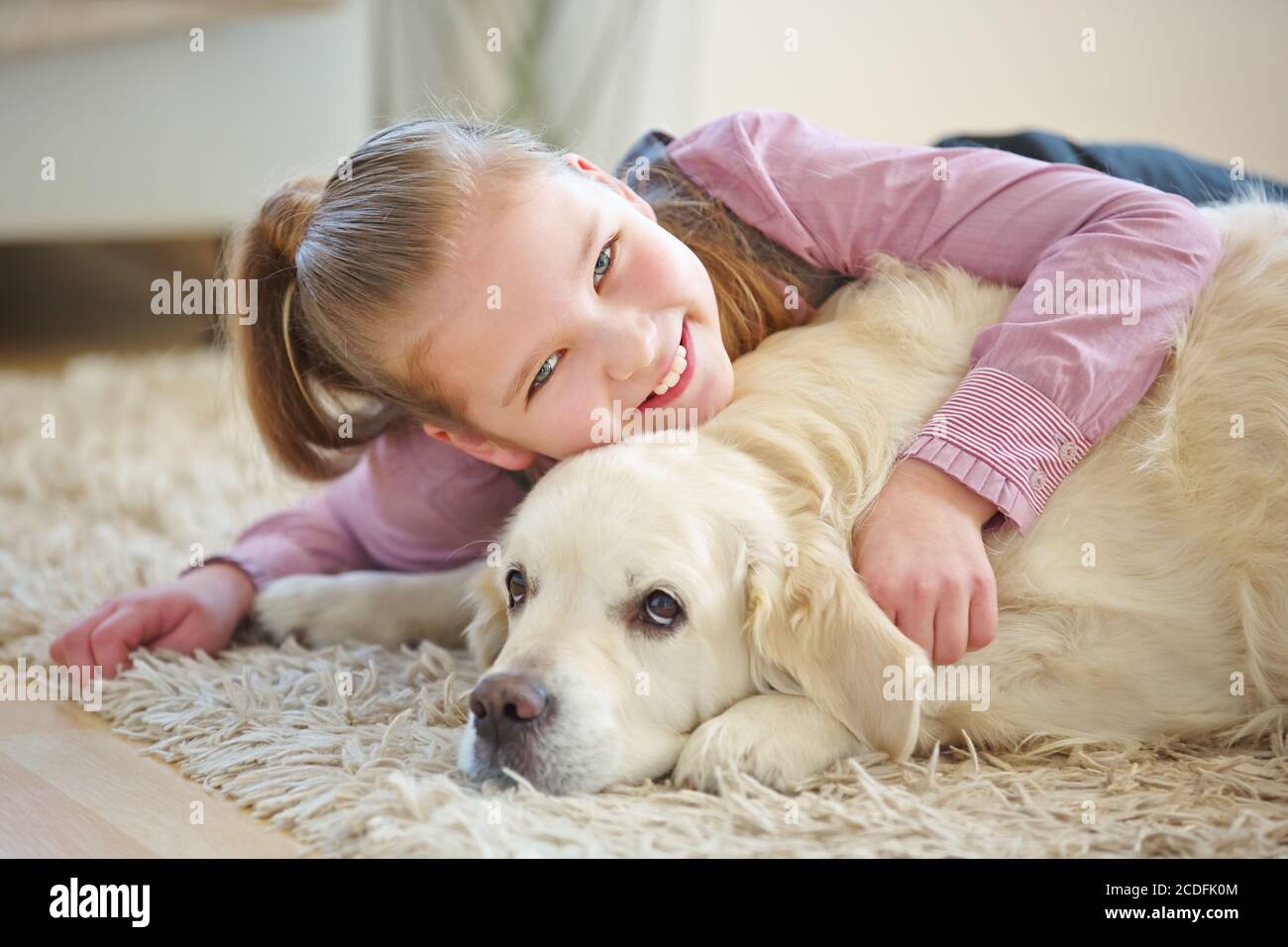 Zufriedenes Kind kuschelt mit goldenem Retriever Hund zu Hause Stockfoto