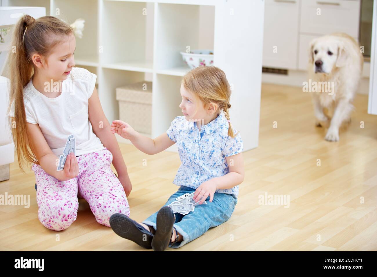 Zwei Kinder spielen Karten zusammen in einem Haus mit einem golden Retriever Hund Stockfoto