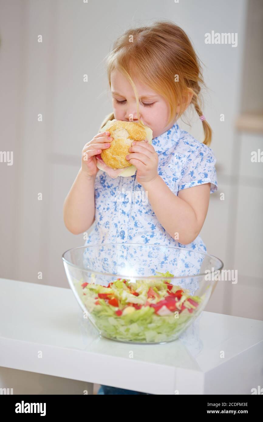 Kind isst Sandwich mit Käse neben Salat in der Küche Stockfoto