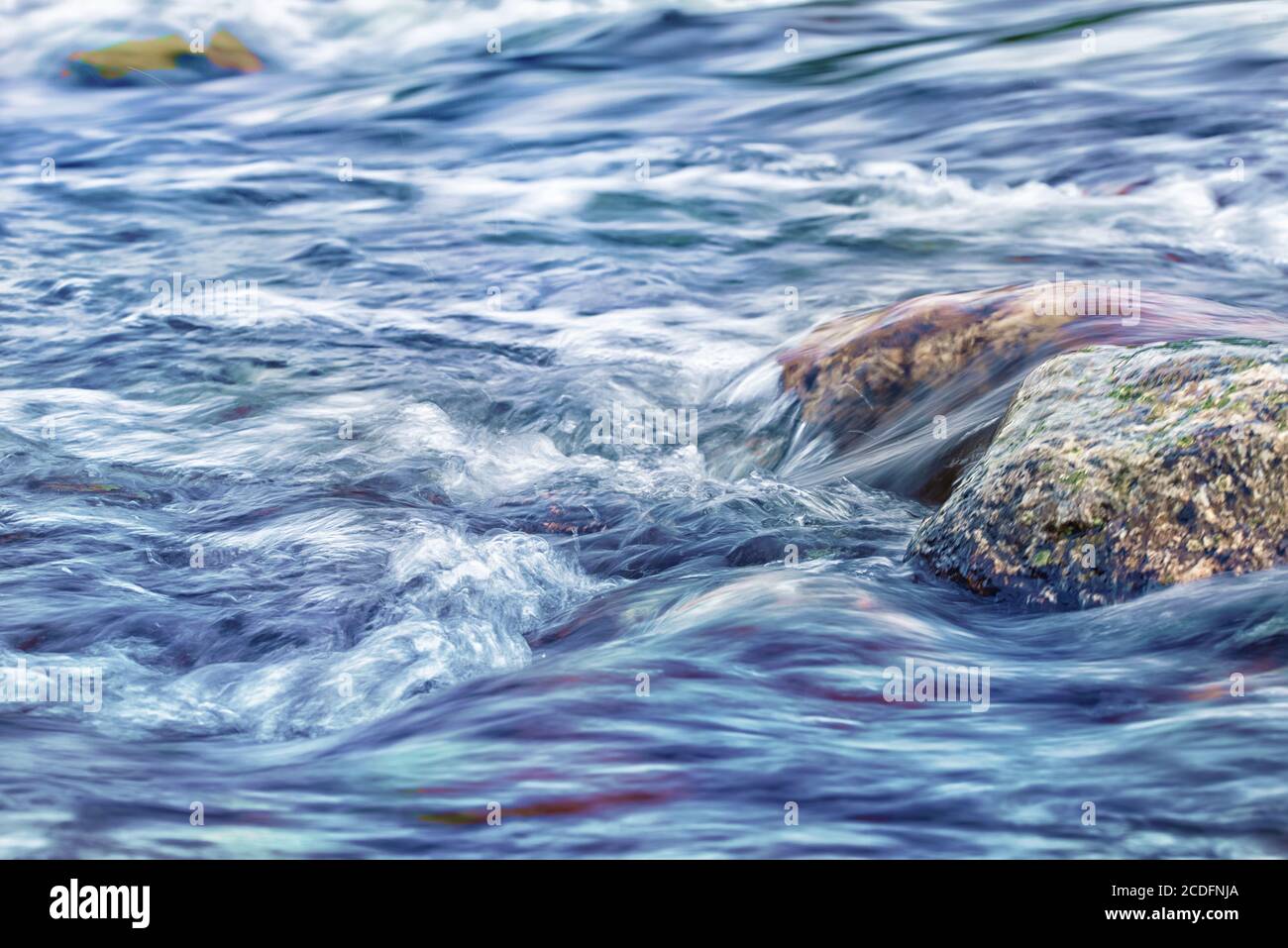 Steine in wild fließenden Fluss. Landschaftsfoto mit Langzeitbelichtung, die das Konzept des Flüssigkeitsflusses darstellt Stockfoto