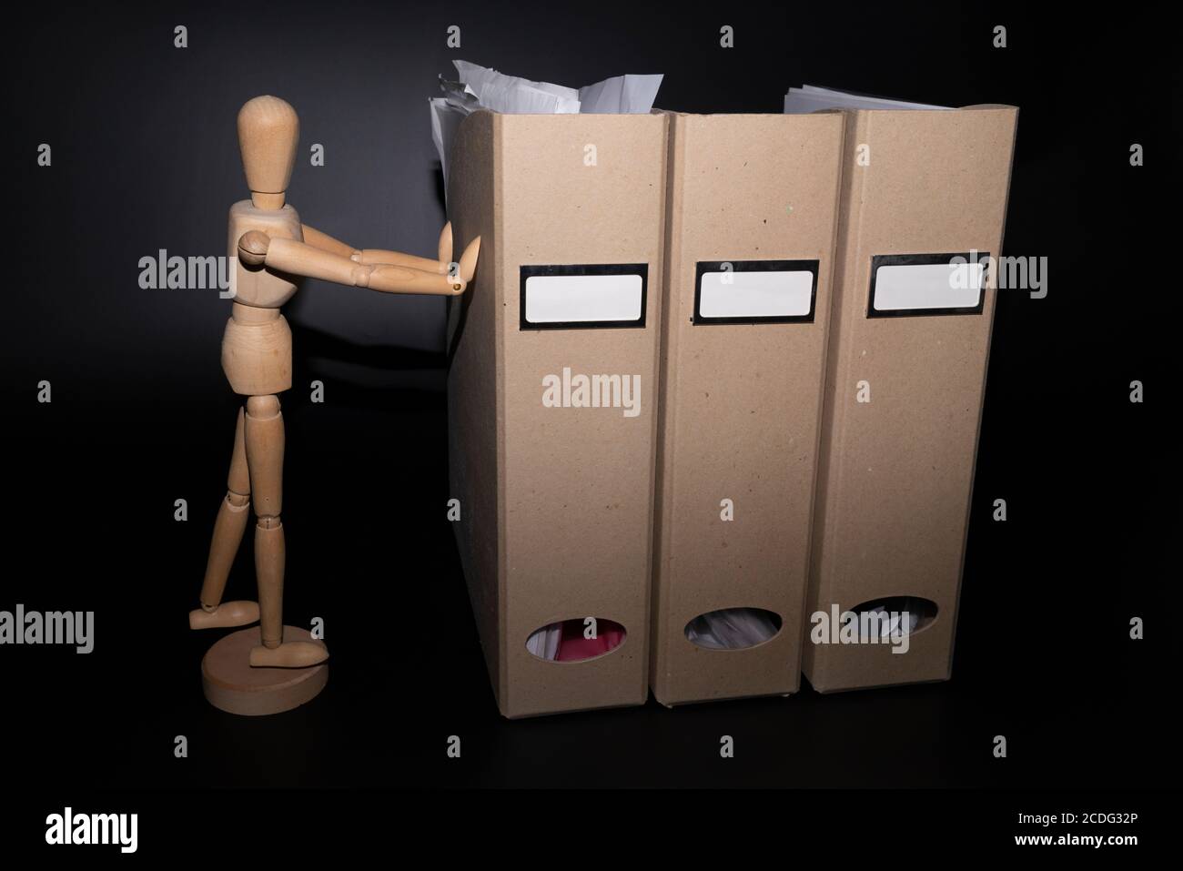 Hölzerne Modellfigur kämpft mit drei braunen Kartons. Stockfoto